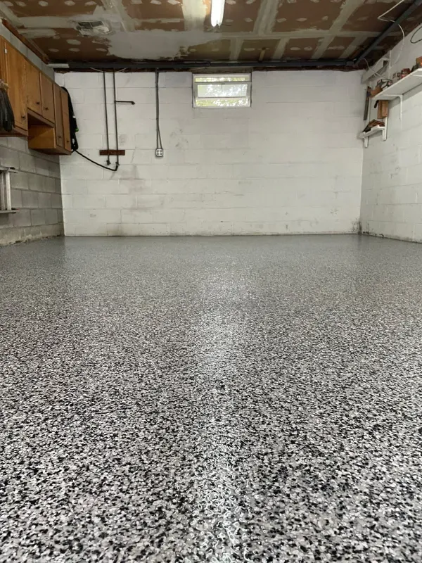Empty garage with speckled epoxy floor, white block walls, and a low ceiling with exposed joists.