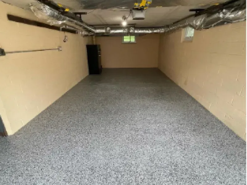 Empty basement room with gray carpet, beige walls, and exposed ceiling fixtures.