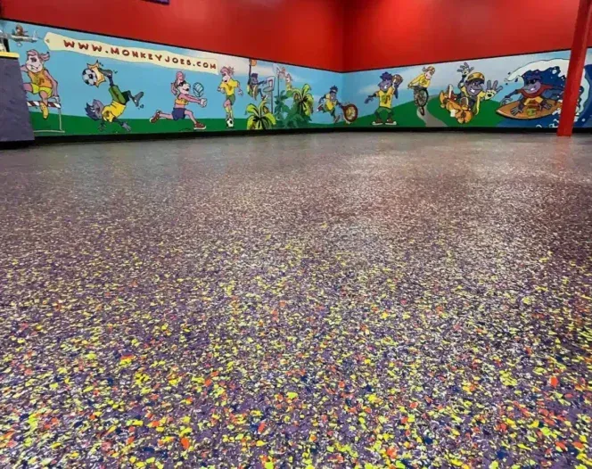 Empty colorful indoor play area with cartoon mural walls and speckled rubber floor