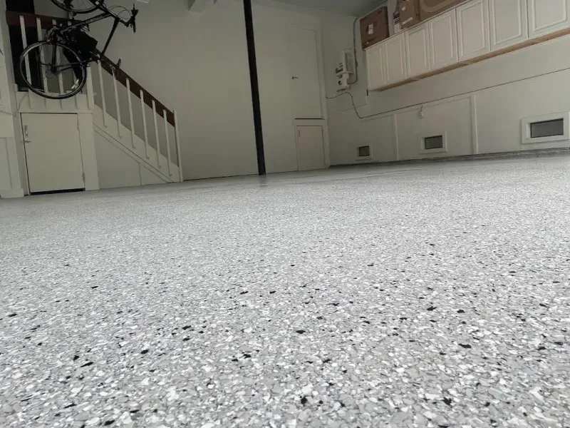 Low-angle view of a speckled white floor in an empty room with stairs and cabinets in the background