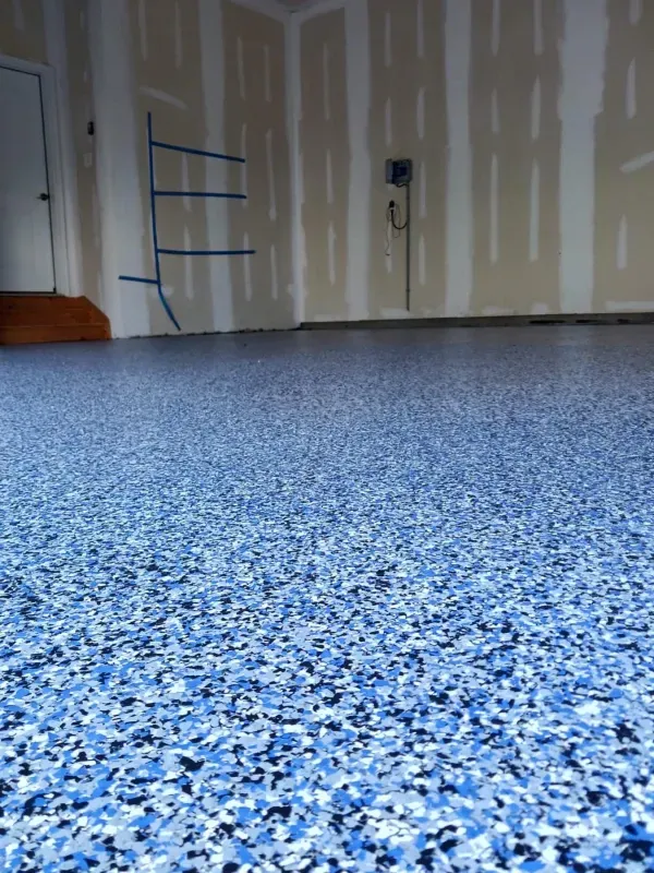 Empty room with blue speckled floor and unfinished drywall, viewed from low angle