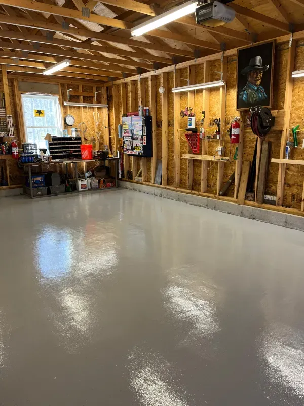 Empty garage with glossy gray floor, exposed wood walls and ceiling, and tools and decor along the right wall