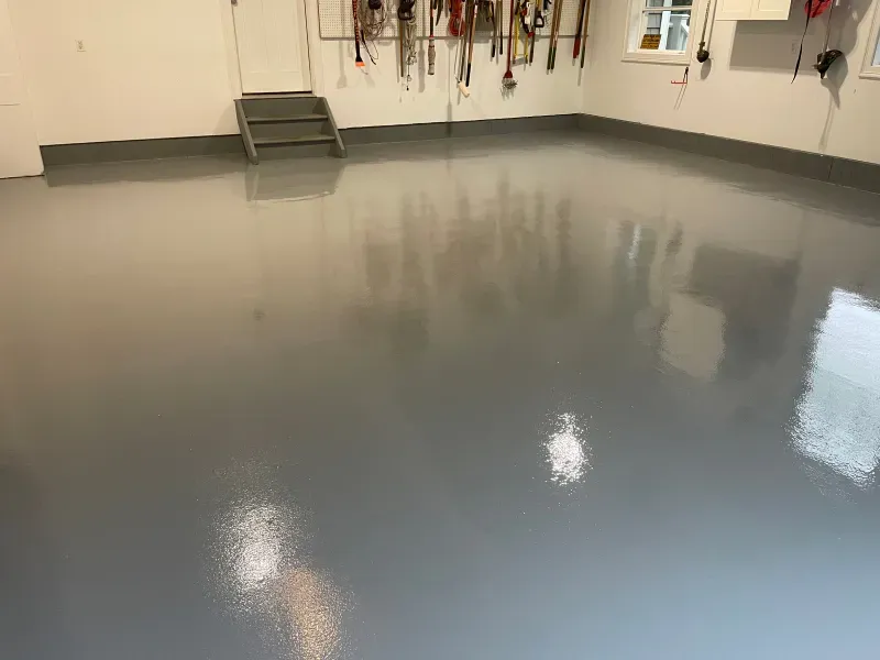 Empty garage with a smooth gray epoxy floor and hanging tools on the wall.