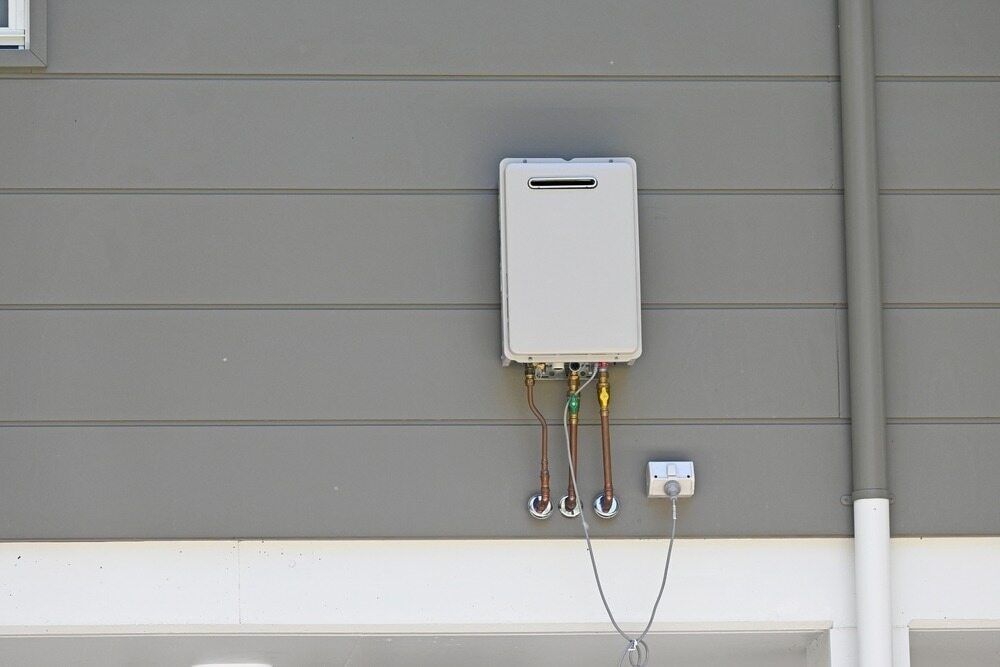A White Water Heater is Attached to the Side of a House — Essential Roofing and Plumbing in Gundagai, NSW