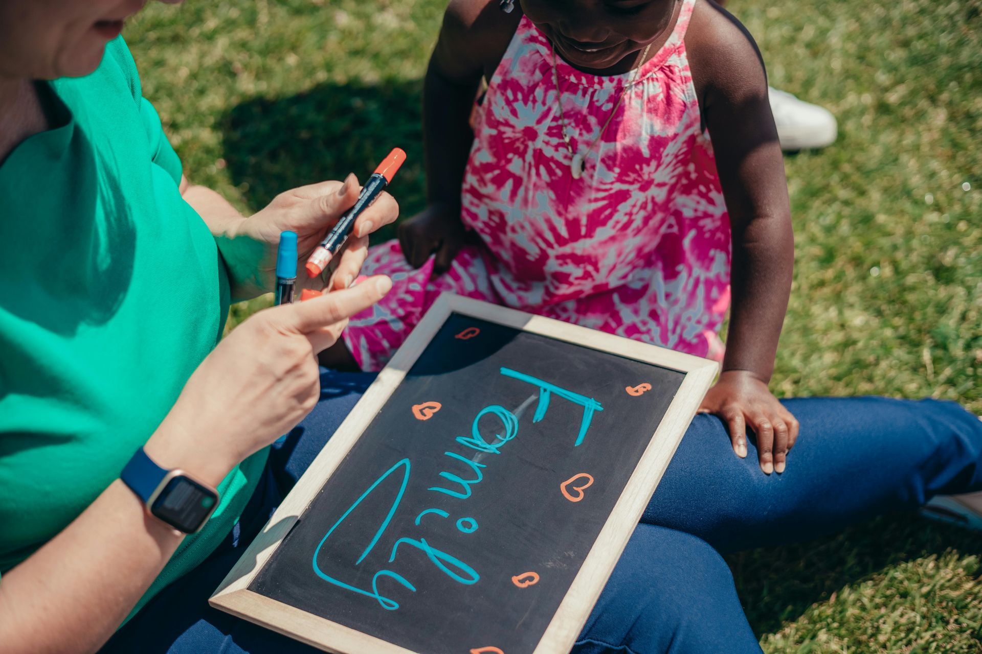 Adult and child drawing on a chalkboard outdoors on grass