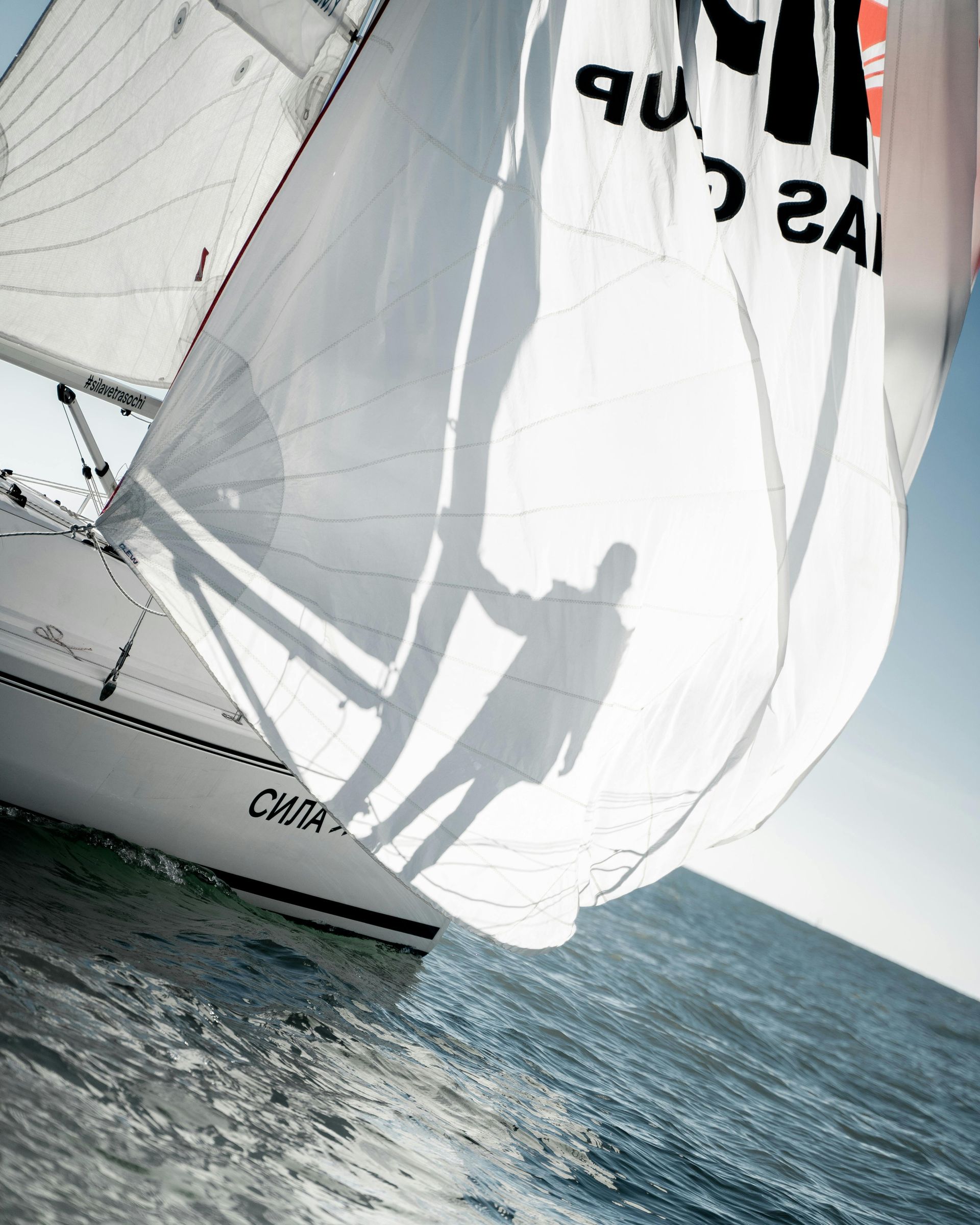 Sailboat with white sails cutting across choppy blue water under bright sunlight