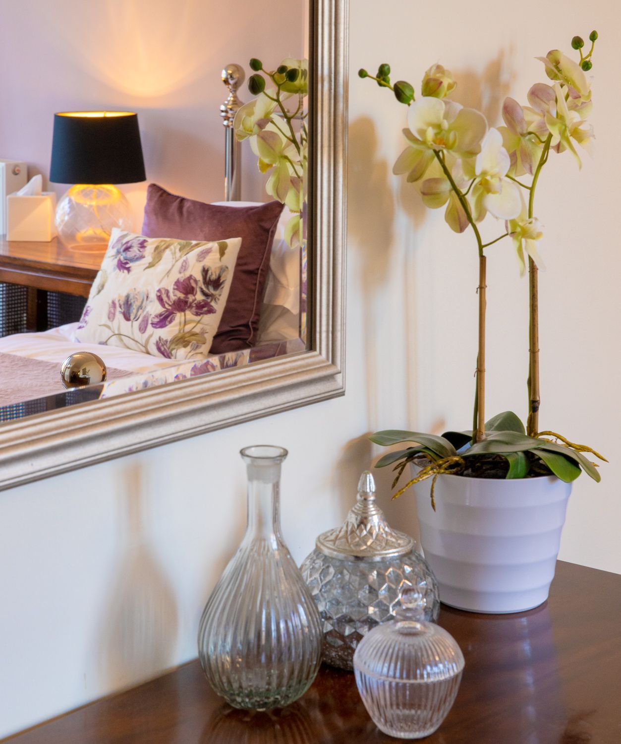 A bedroom with a mirror and a vase of flowers on a table.