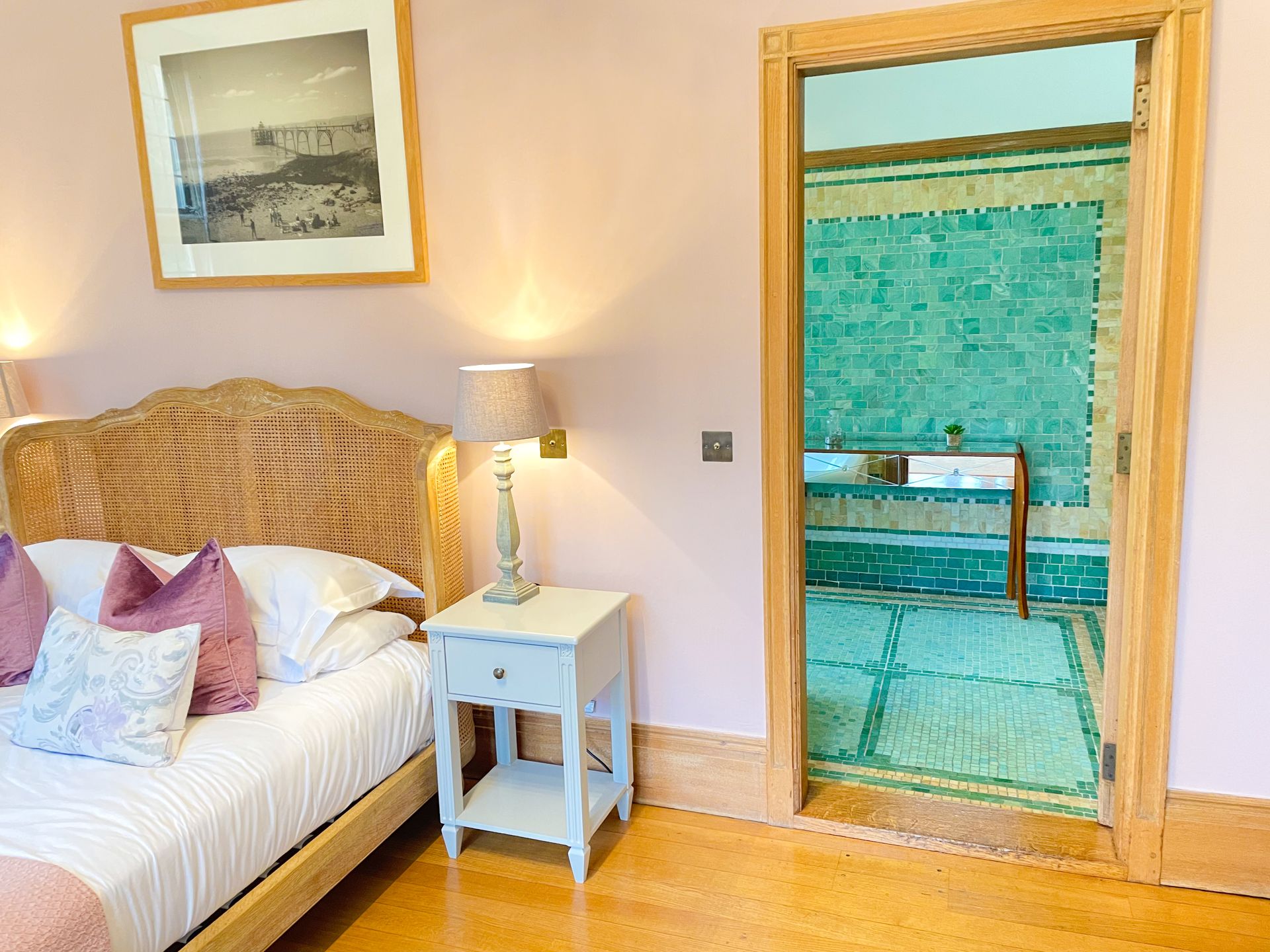 A bedroom with a bed , nightstand , lamp and a door leading to a bathroom.