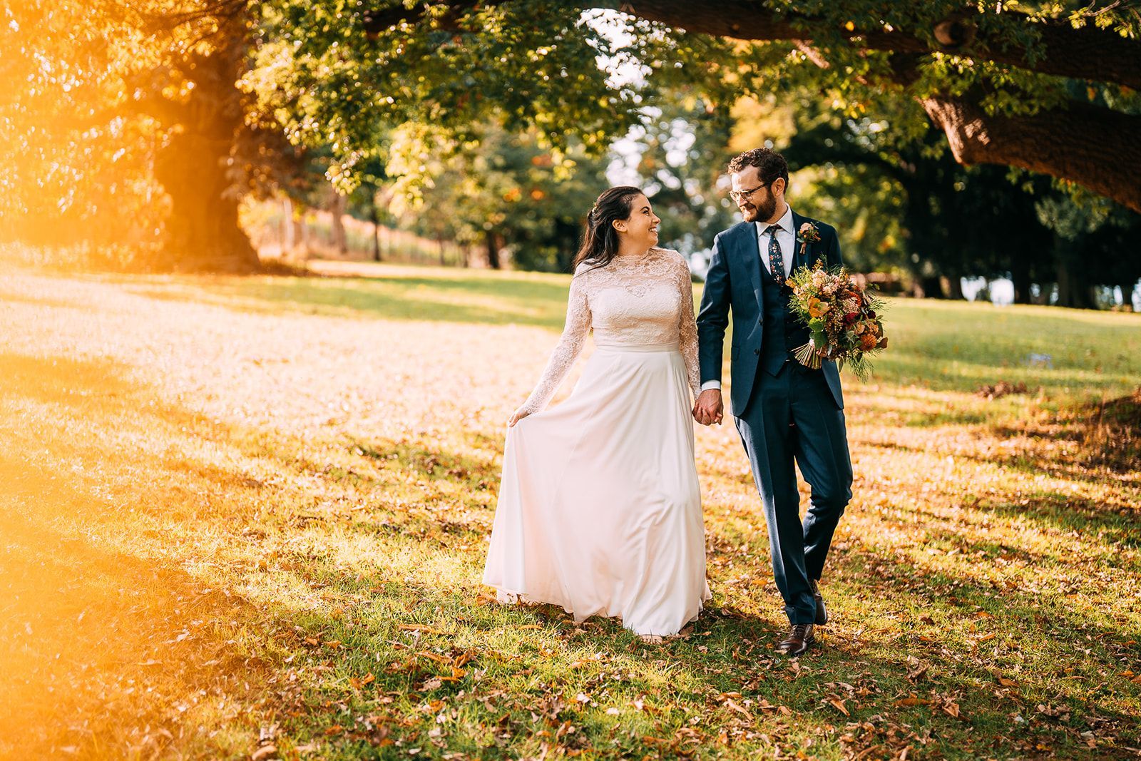 A bride and groom are walking in a park holding hands.