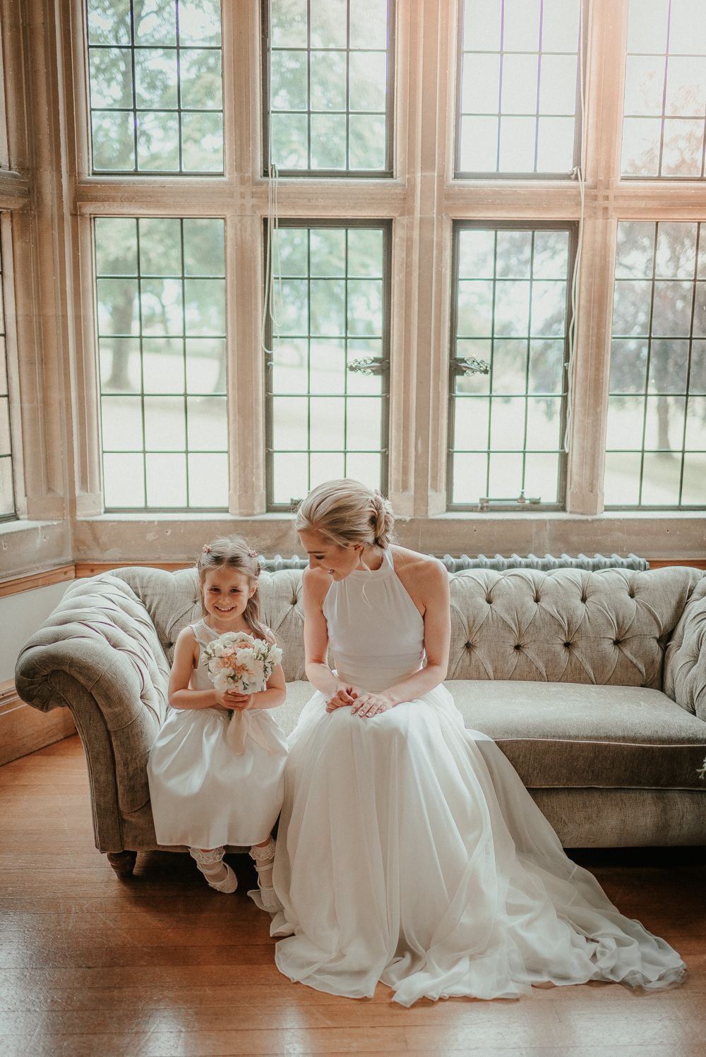 A bride and a flower girl are sitting on a couch.