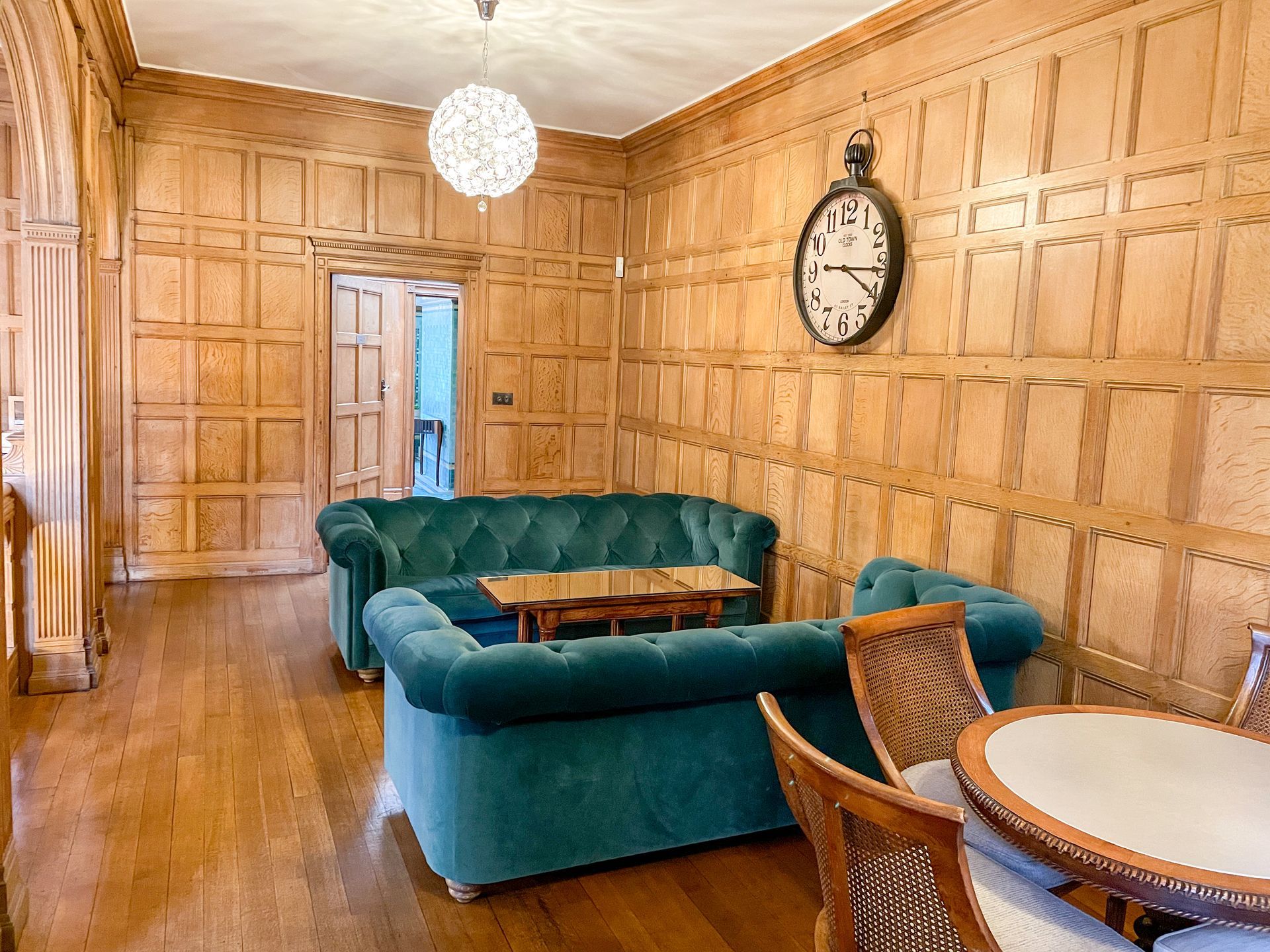 A living room with a couch , table , chairs and a clock on the wall.