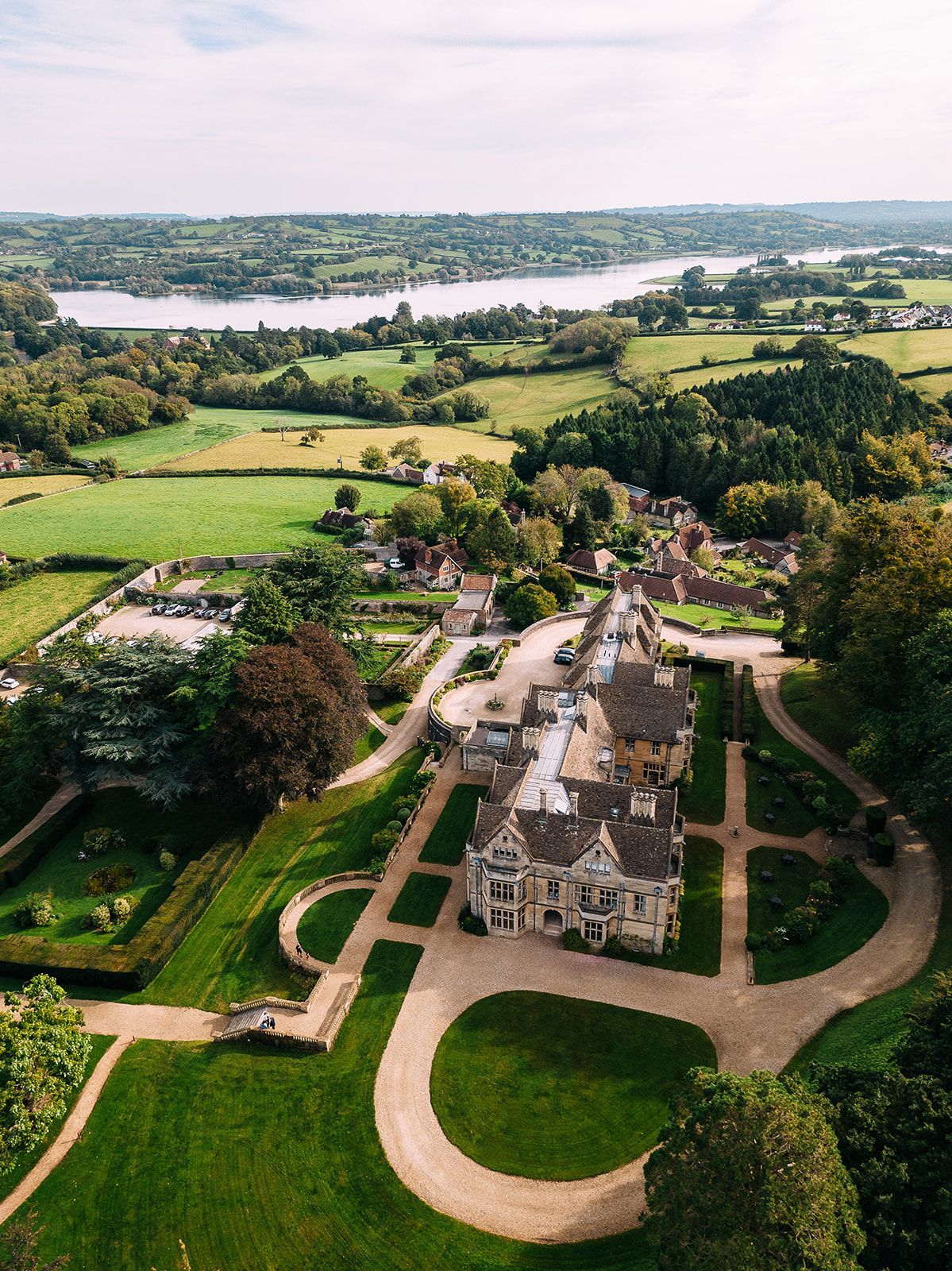 An aerial view of a large house in the middle of a lush green field surrounded by trees.
