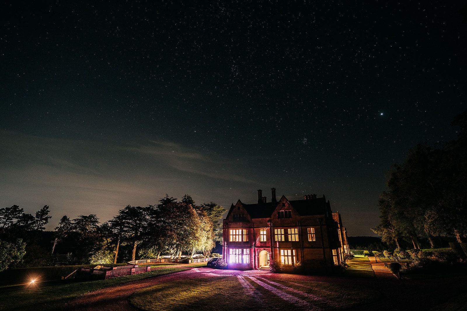 A large house is lit up at night under a starry sky.