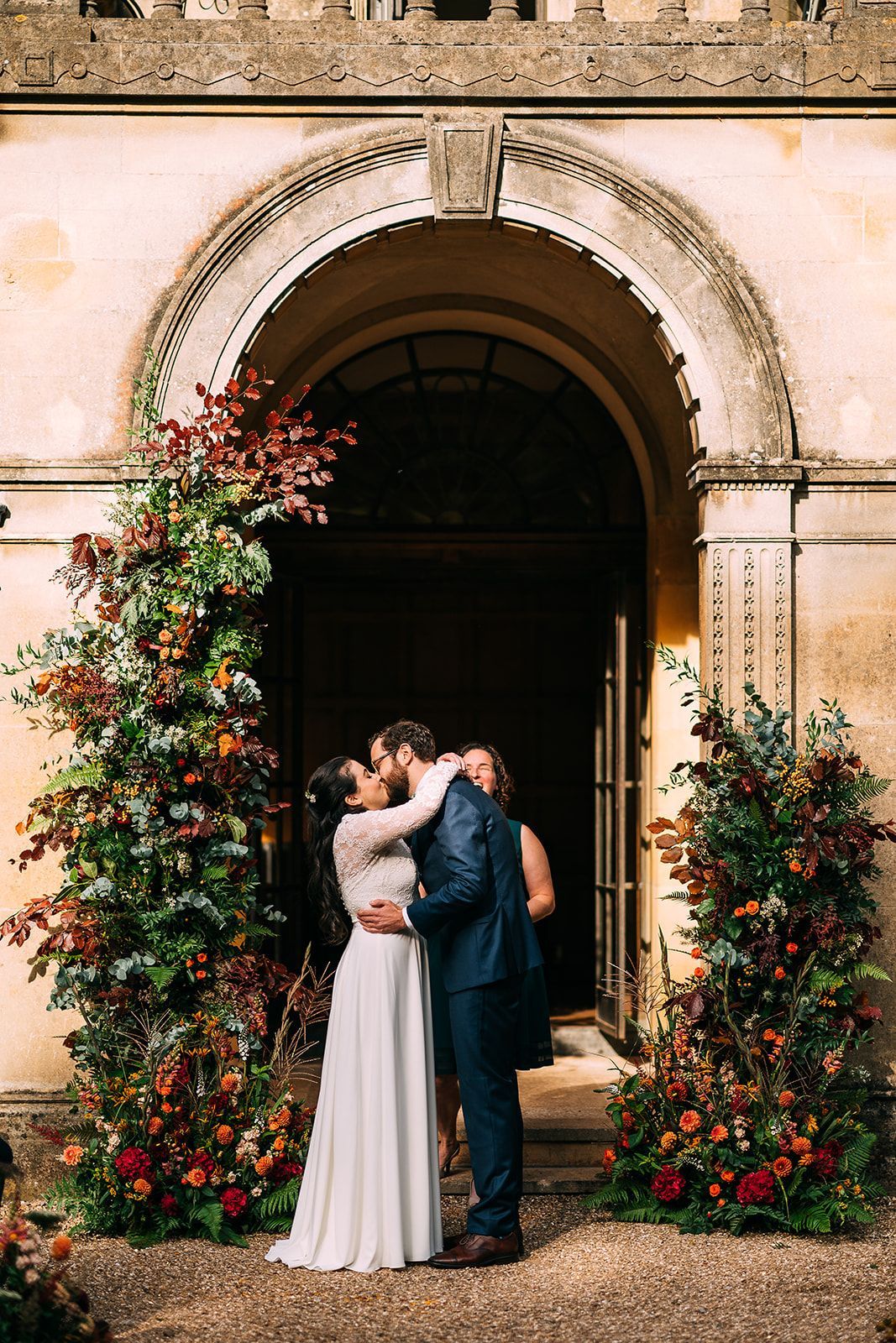 A bride and groom kissing in front of a building with flowers.