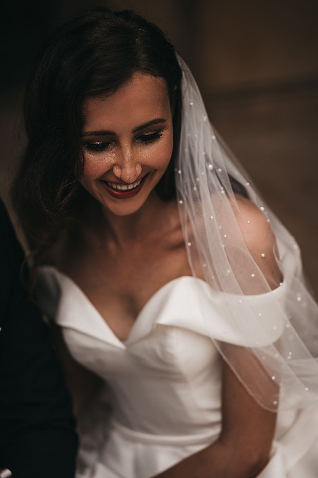 The bride is wearing a veil and smiling while sitting next to the groom.