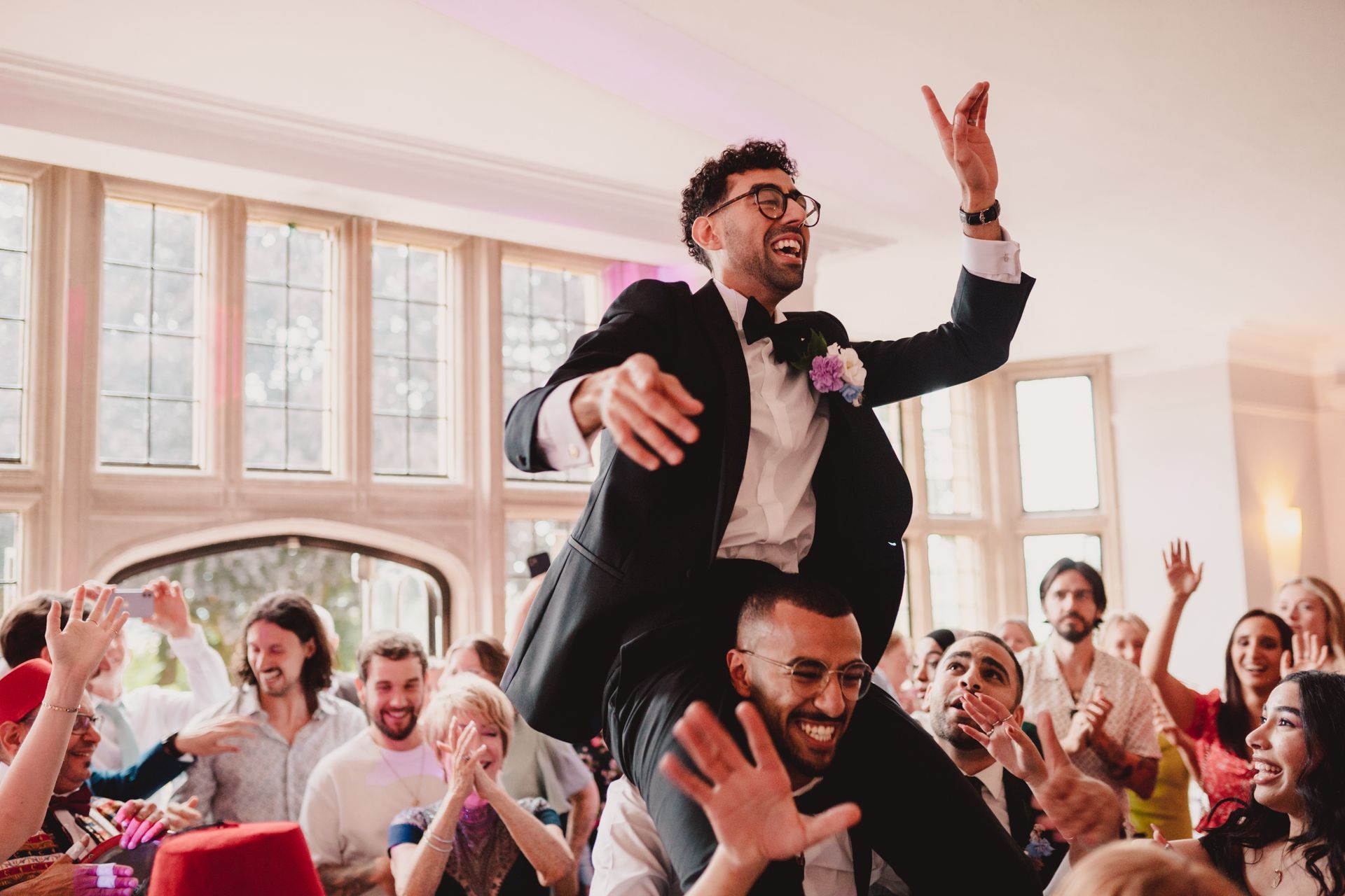 A man in a suit is being lifted in the air by another man at a wedding reception.