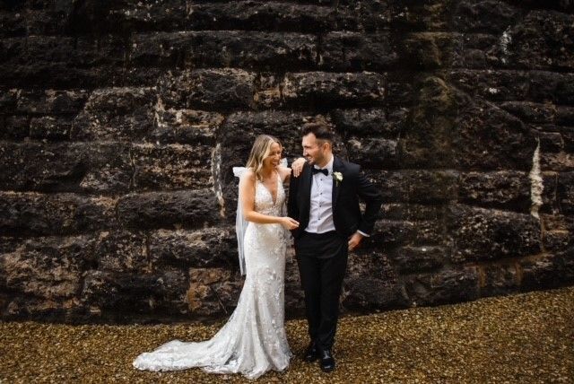 A bride and groom are standing next to each other in front of a brick wall.