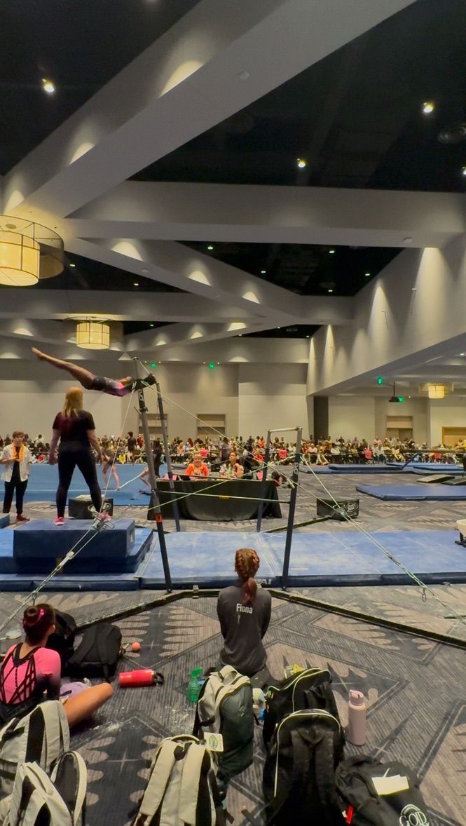 Gymnast in mid-air performing a routine on uneven bars, audience watching in a large indoor venue.