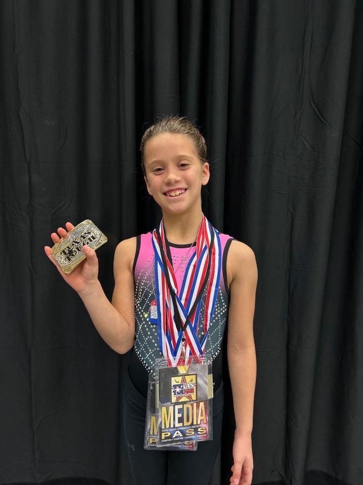 Gymnast holding medals, smiling, wearing a leotard and a 