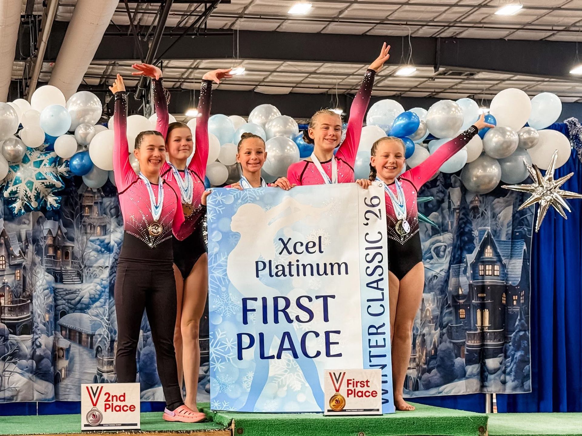 Gymnasts celebrate a first-place win at the Xcel Platinum Winter Classic '26, raising arms with medals,