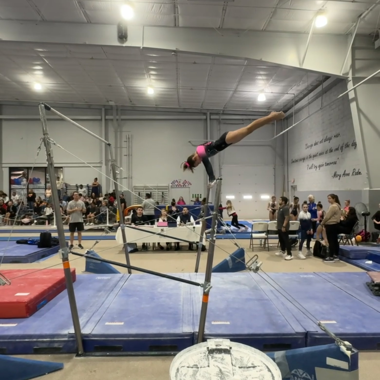 Gymnast on uneven bars performing a handstand. Competition setting, audience present.