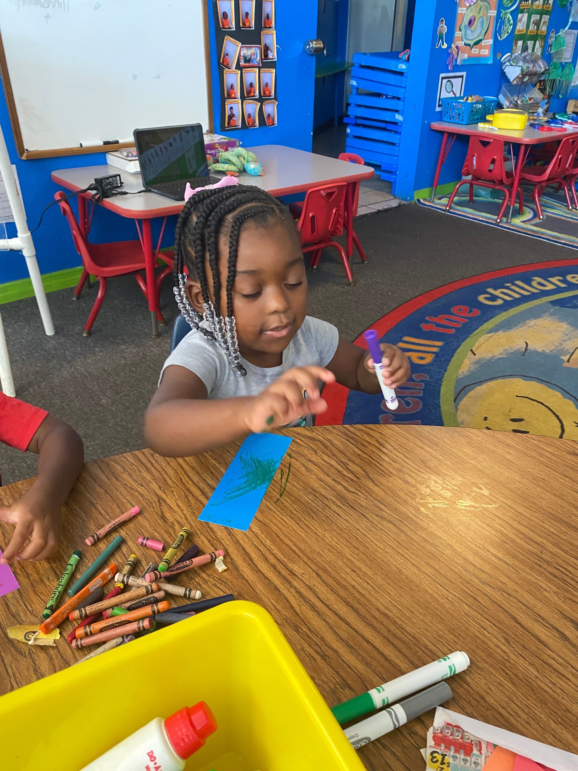 A little girl is sitting at a table in a classroom holding a marker.