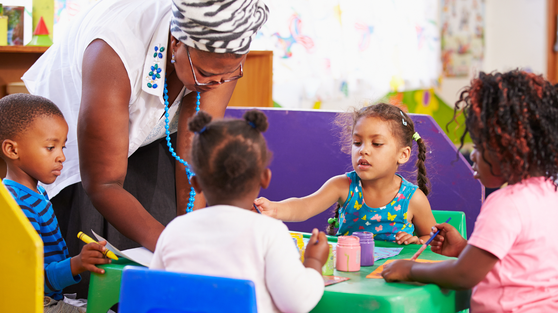 A woman is teaching a group of children at a table in a classroom.