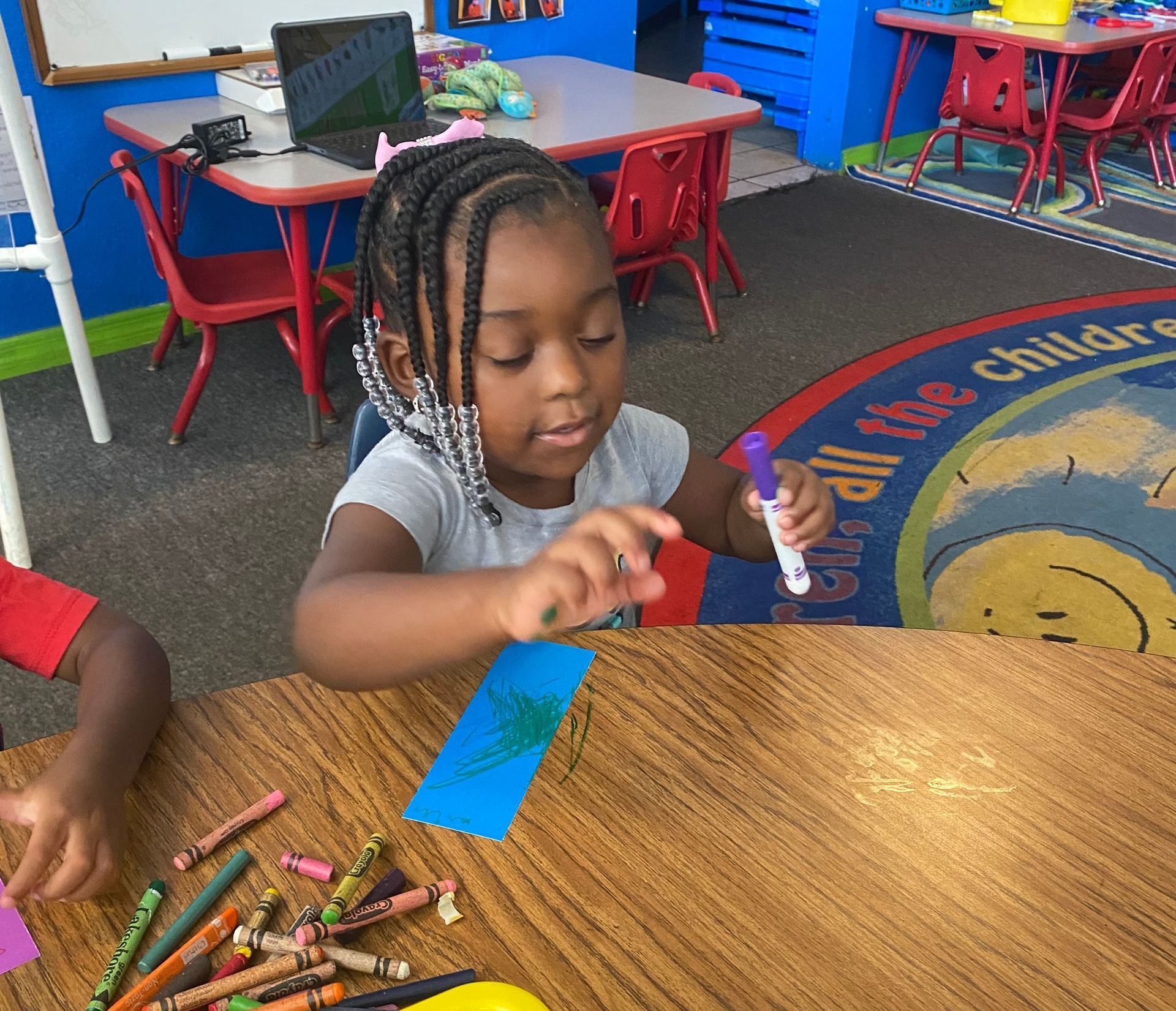 A little girl is sitting at a table holding a marker.