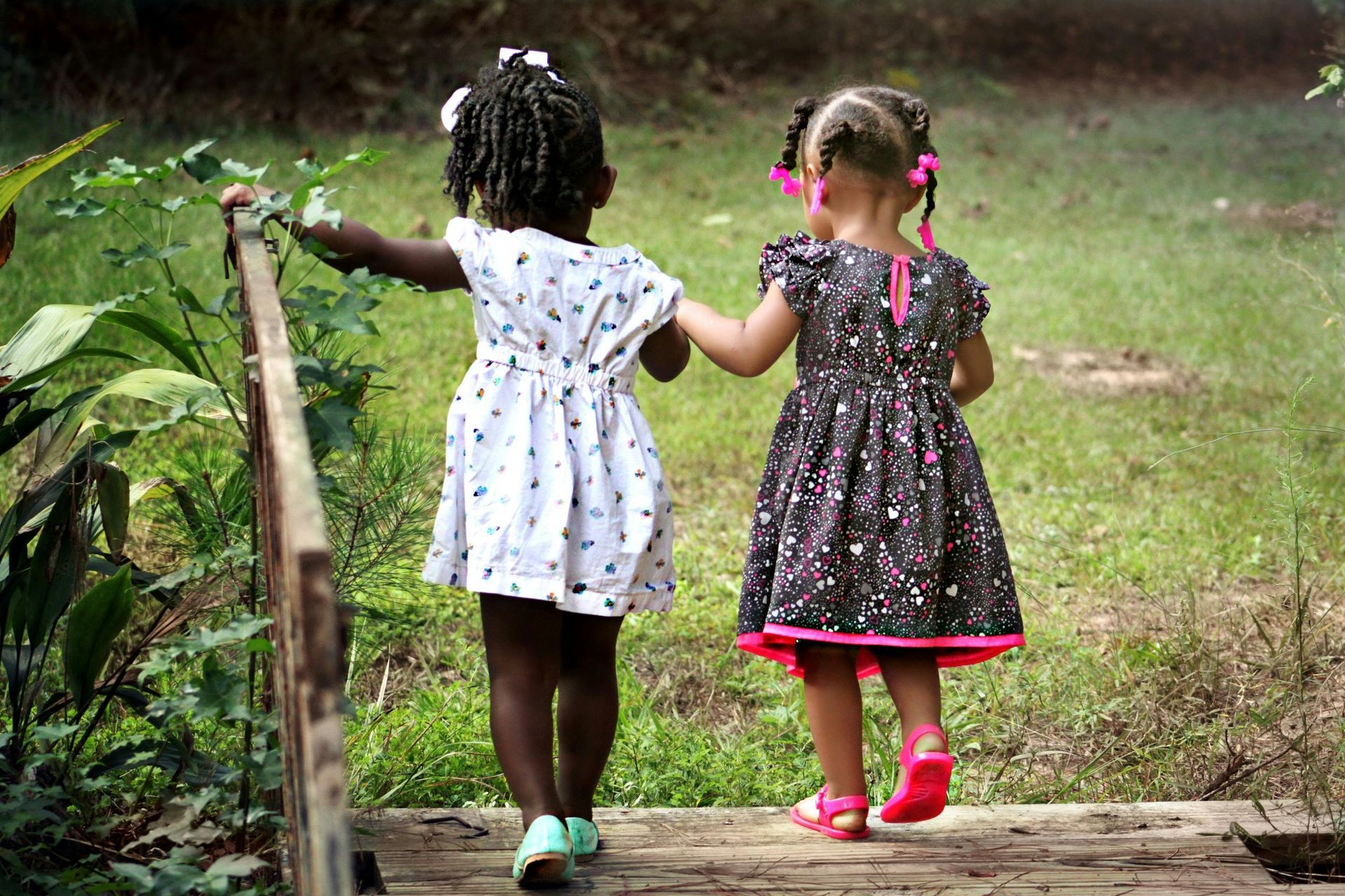 Two little girls are walking across a wooden bridge holding hands.