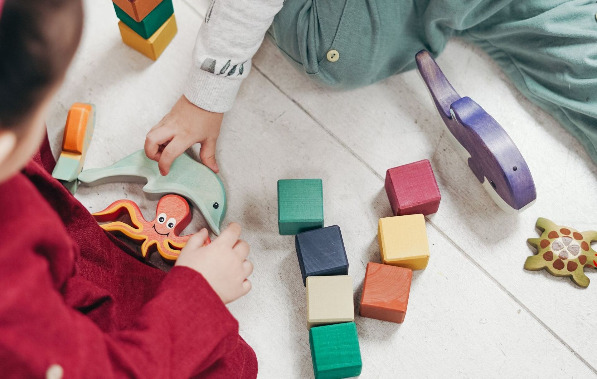 Two children are playing with wooden blocks on the floor.