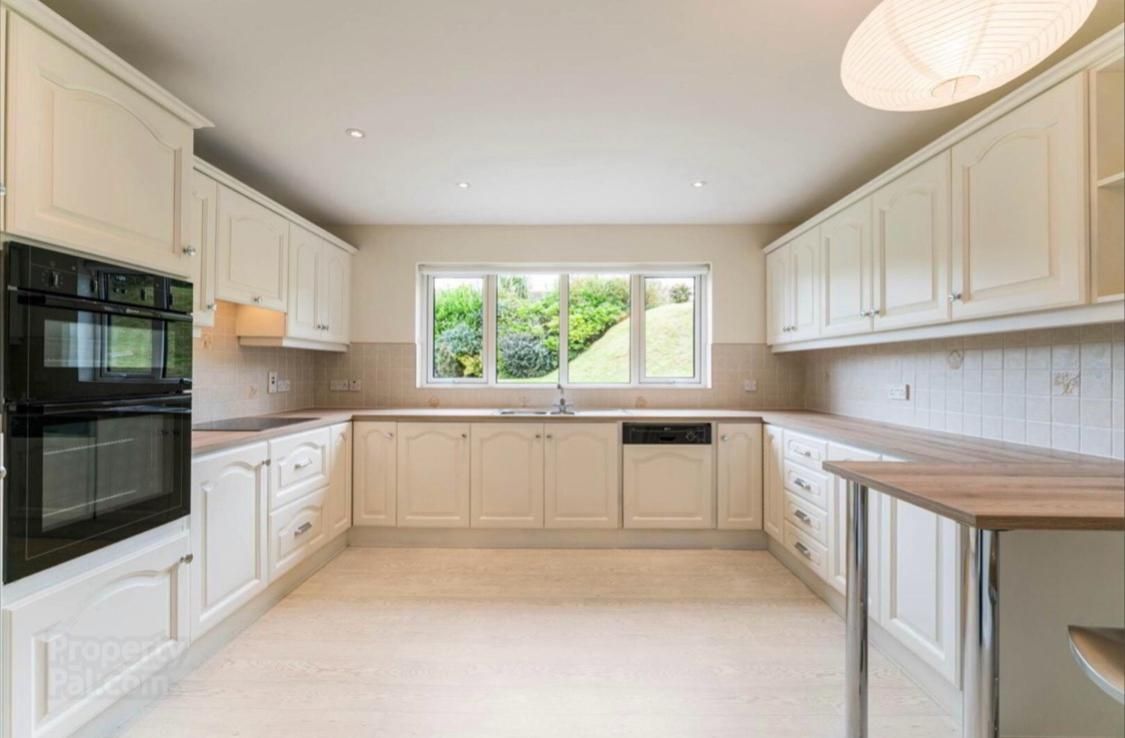an empty kitchen with white cabinets , a black oven , a sink , and a window .