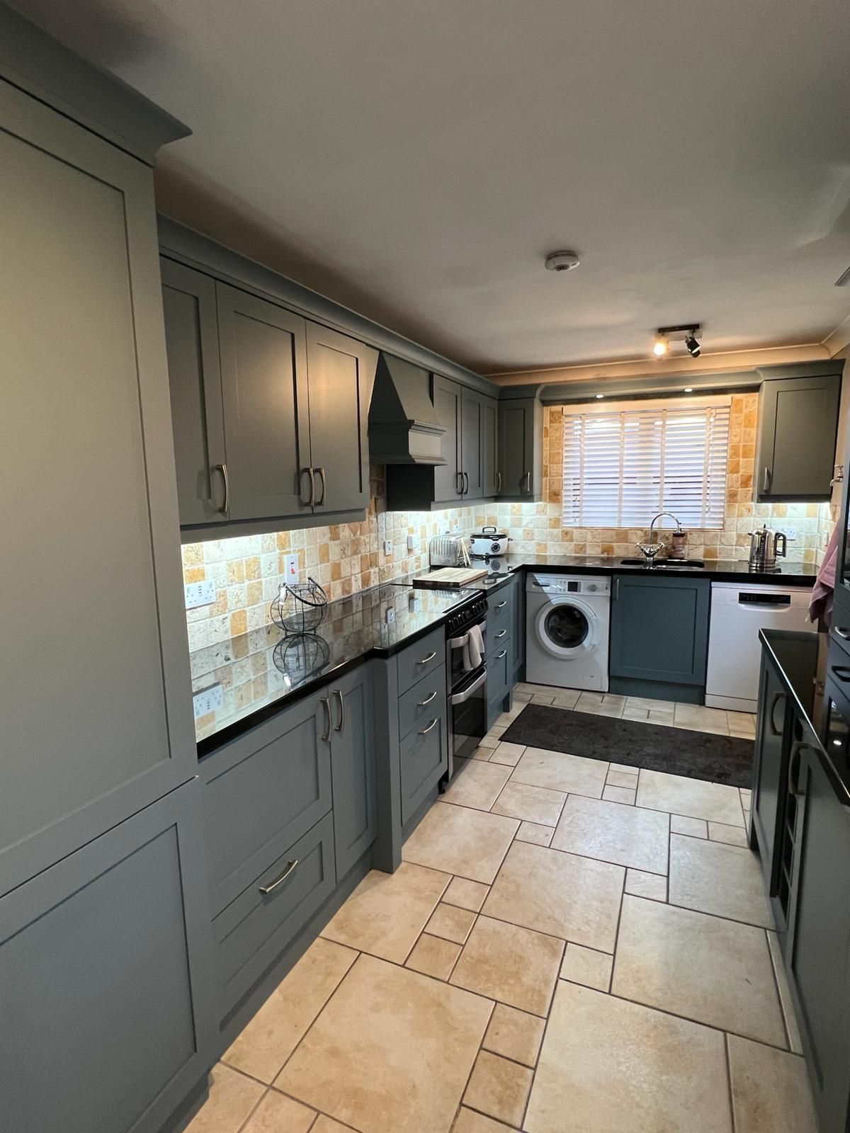 a kitchen with gray cabinets , black counter tops , a washer and dryer , and a window .