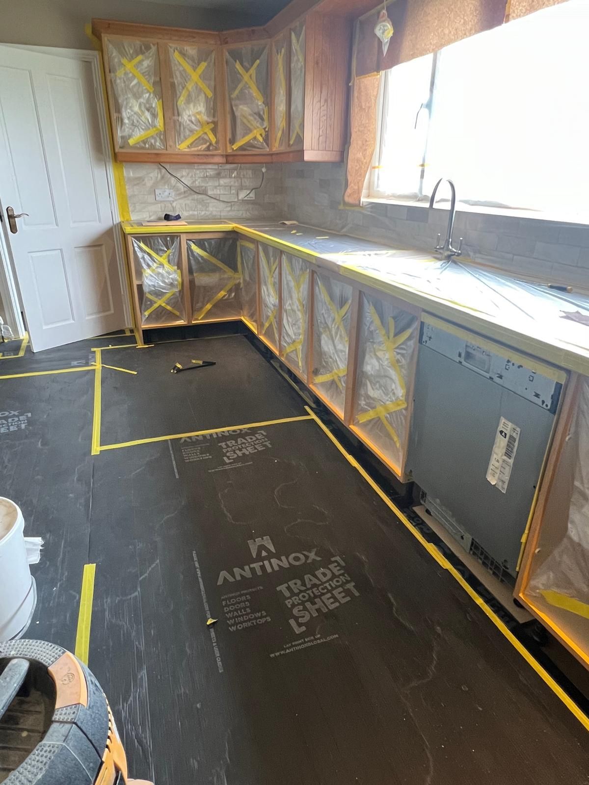 A kitchen is being remodeled with a rubber sheet on the floor.