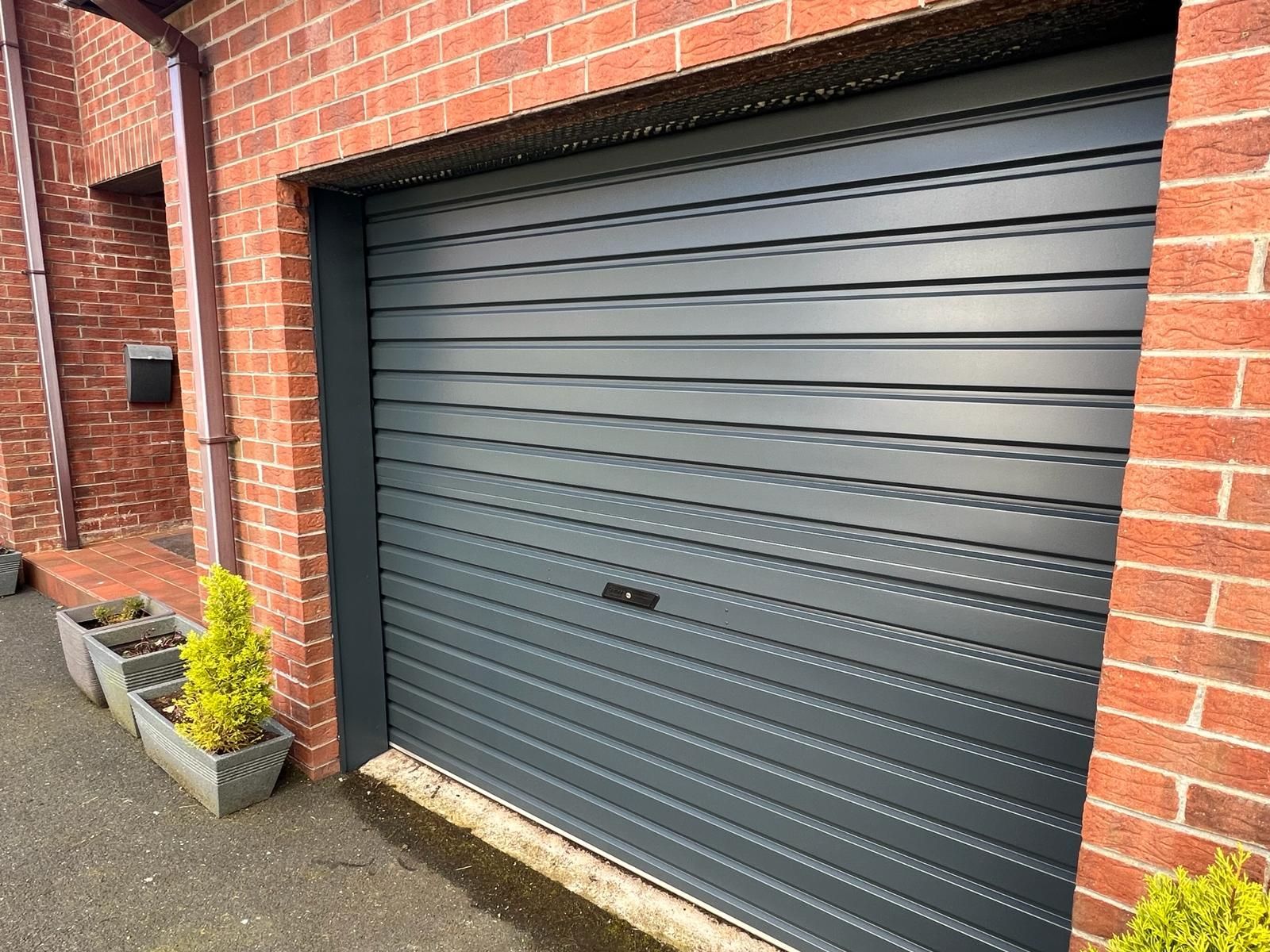 a black garage door is sitting in front of a brick building .