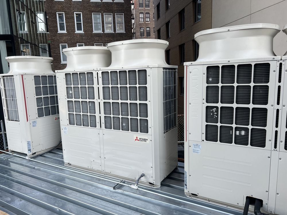 A row of white outdoor commercial HVAC air conditioning units positioned on a metal rooftop against a city building.