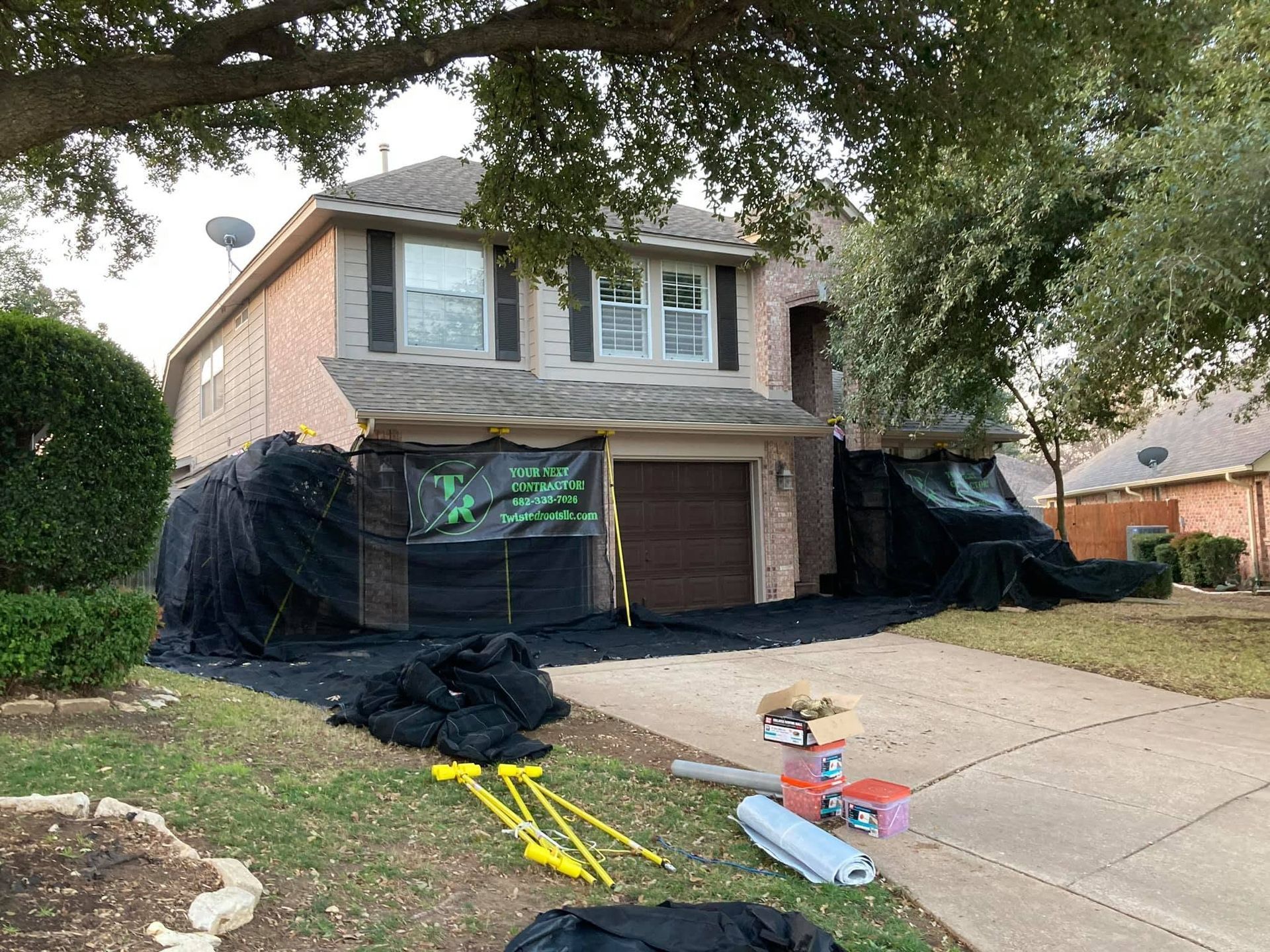 Two-story house with black tarps and construction materials in the driveway and yard.