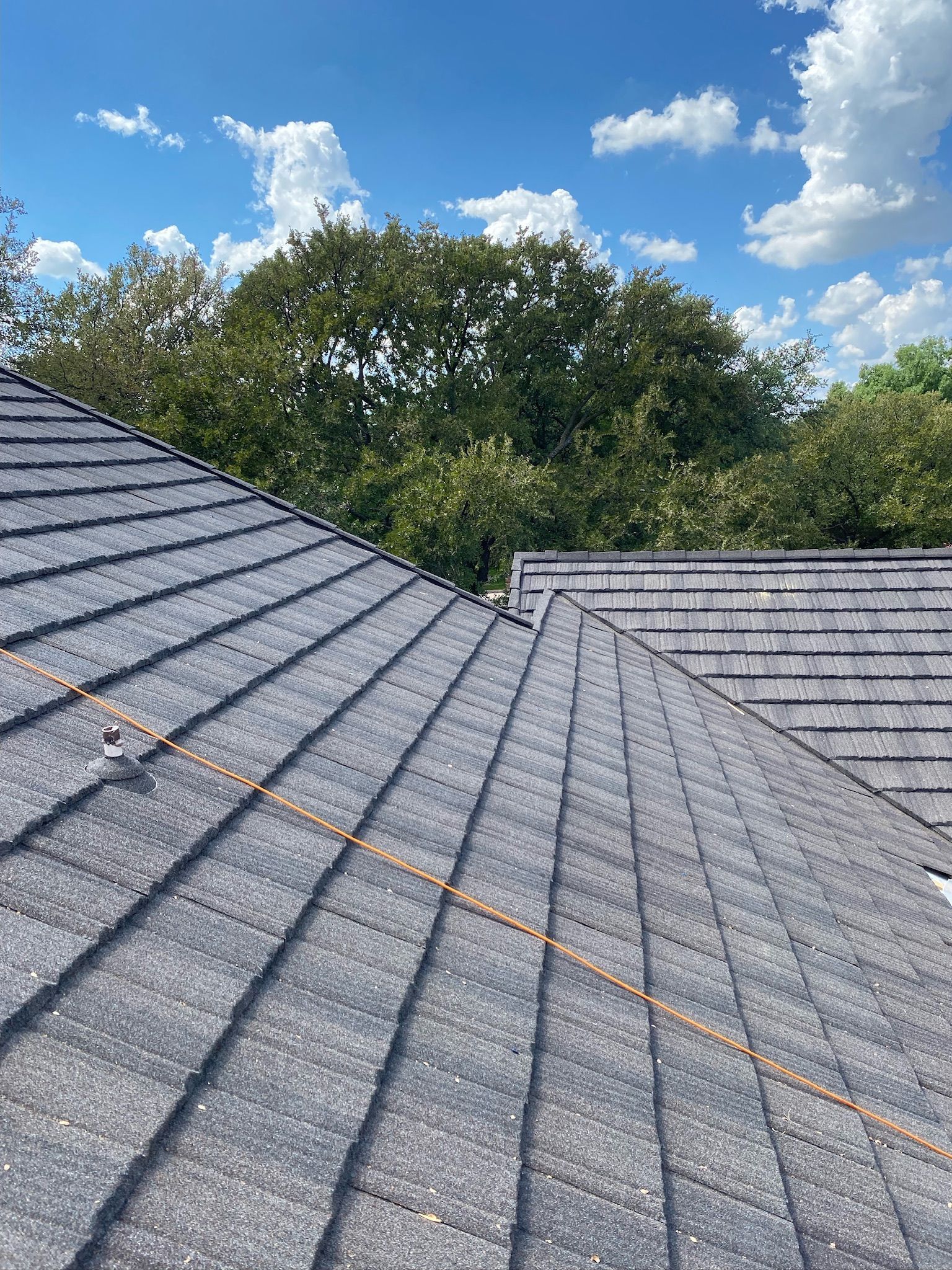 Gray shingle roof under a bright blue sky with trees in the background
