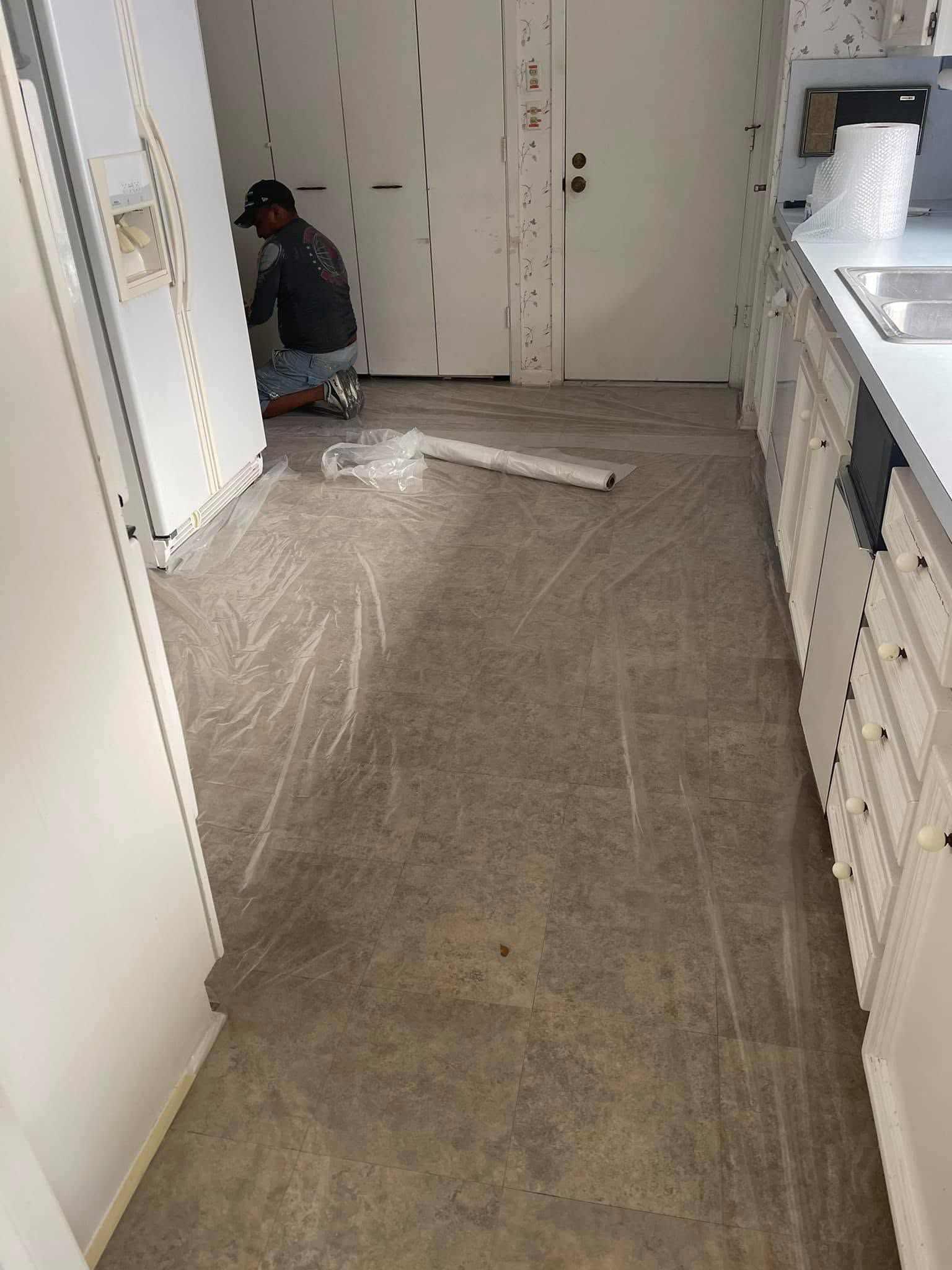 Man kneeling on a plastic-covered floor in a narrow kitchen under renovation