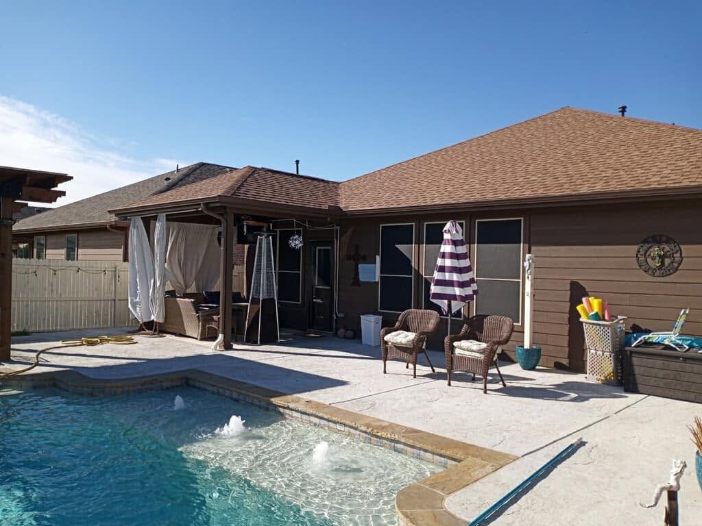 Backyard pool patio with beige house, umbrella, chairs, and covered patio area