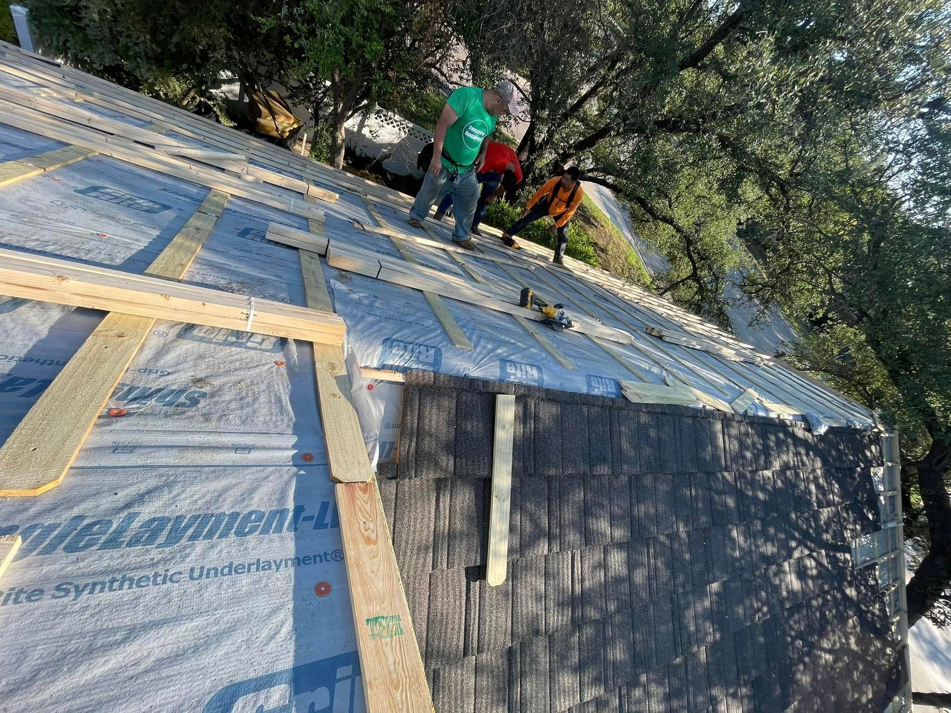 Workers installing roofing sheets on a sloped roof, with trees in the background.