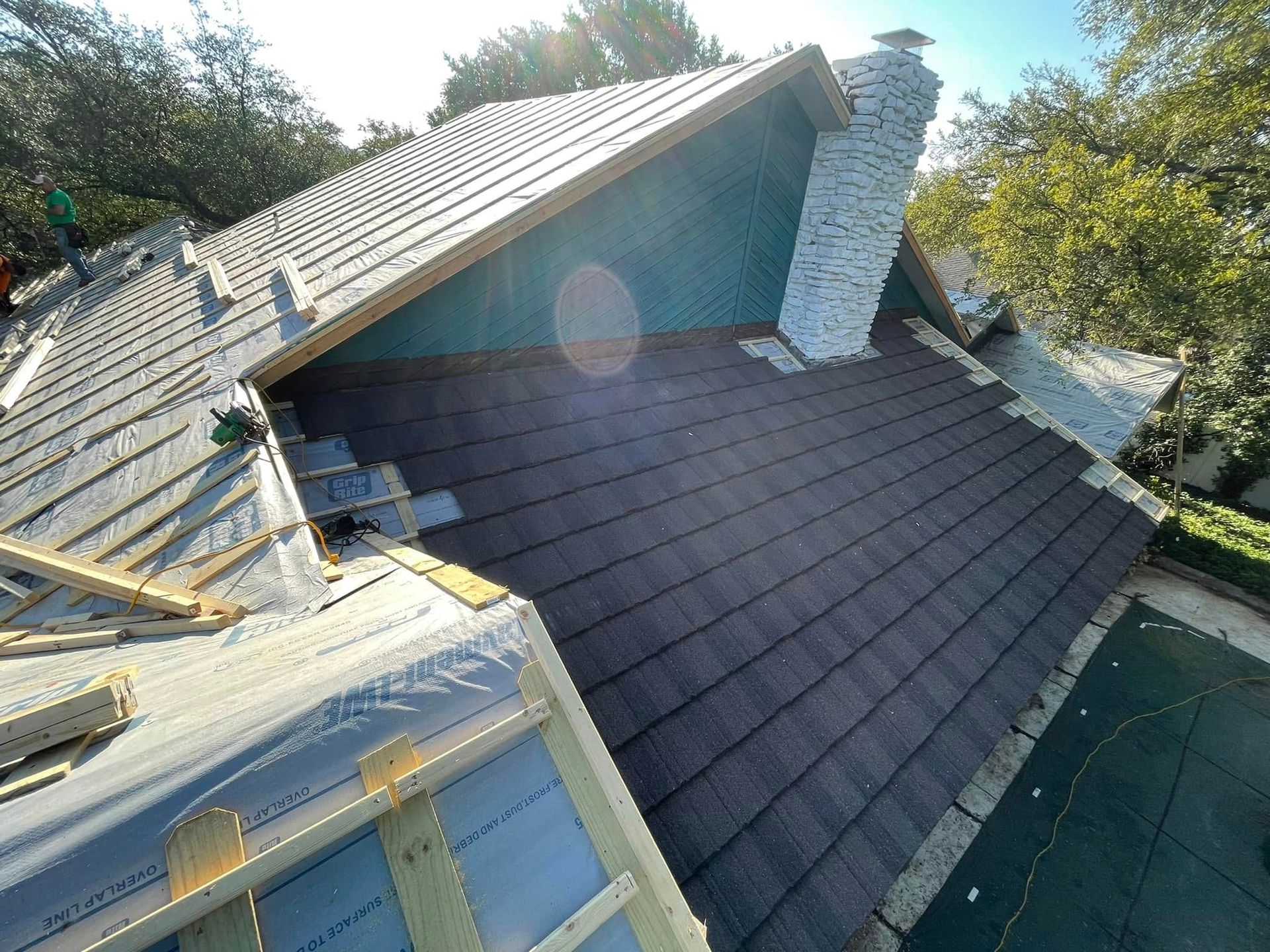 Roofing work on a house with dark shingles and a white chimney under bright sunlight