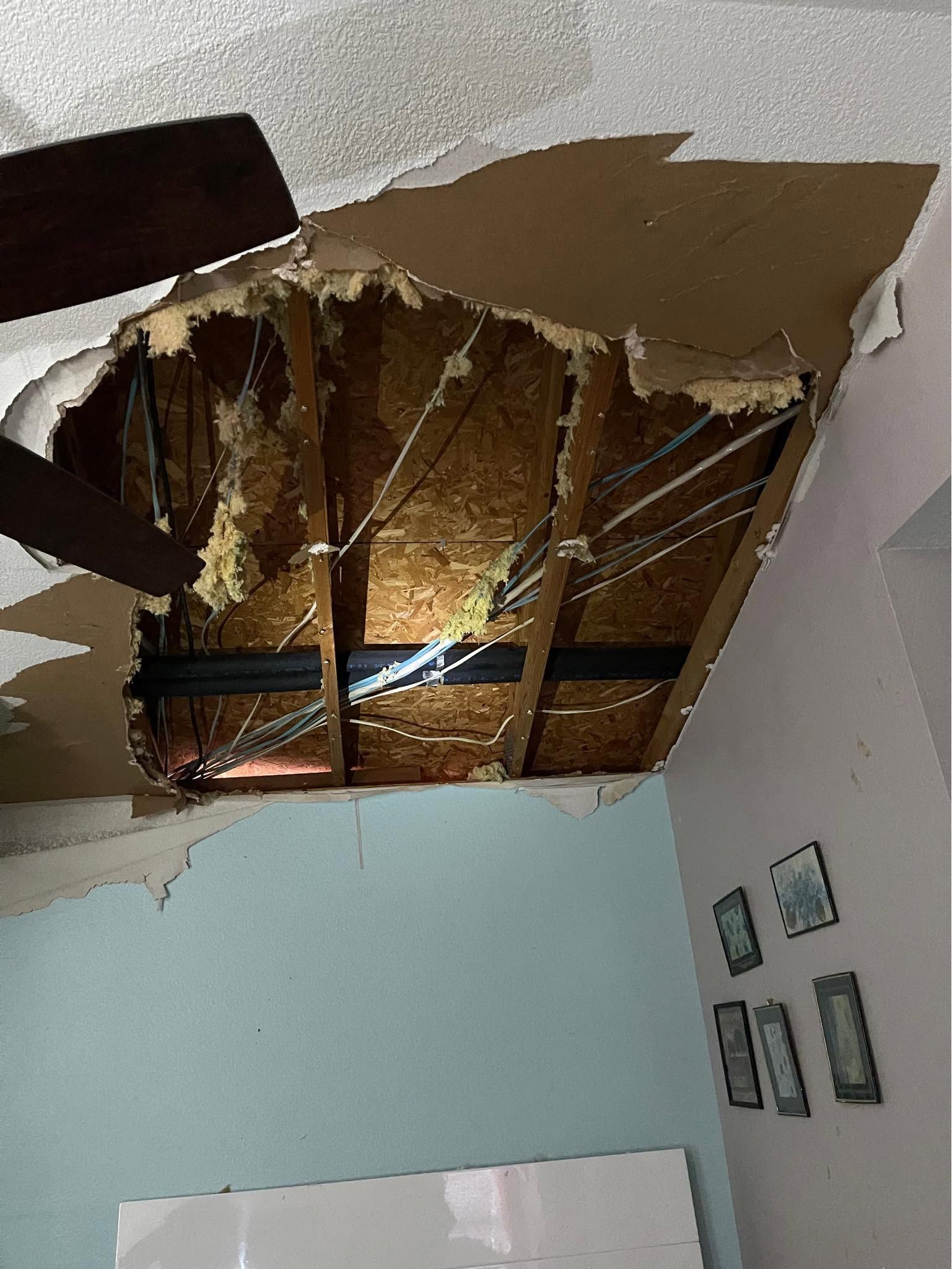 Damaged ceiling with large torn section exposing wooden beams in a light blue room