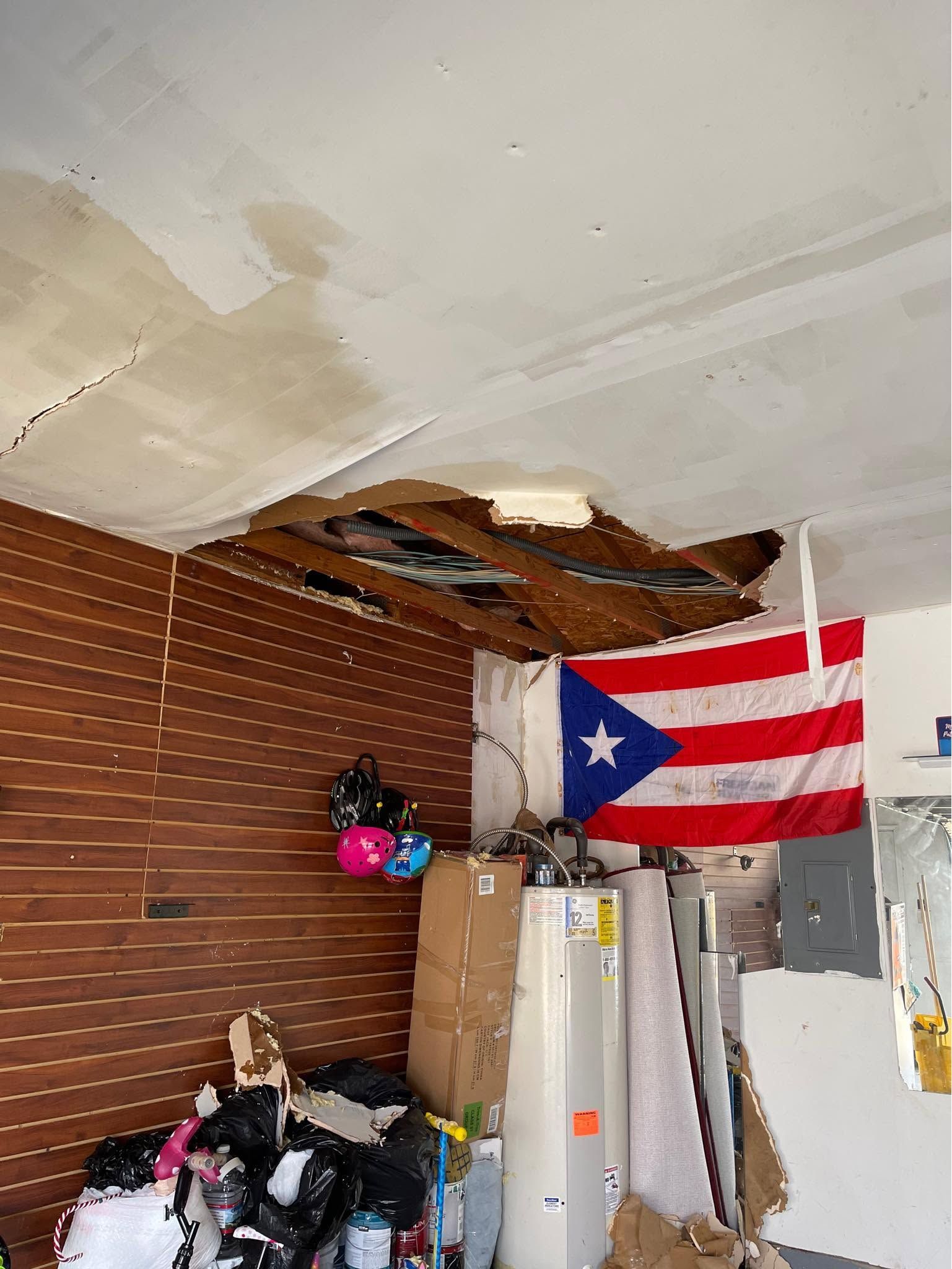 Damaged ceiling above stacked boxes and refrigerator, with a Puerto Rican flag on the wall.