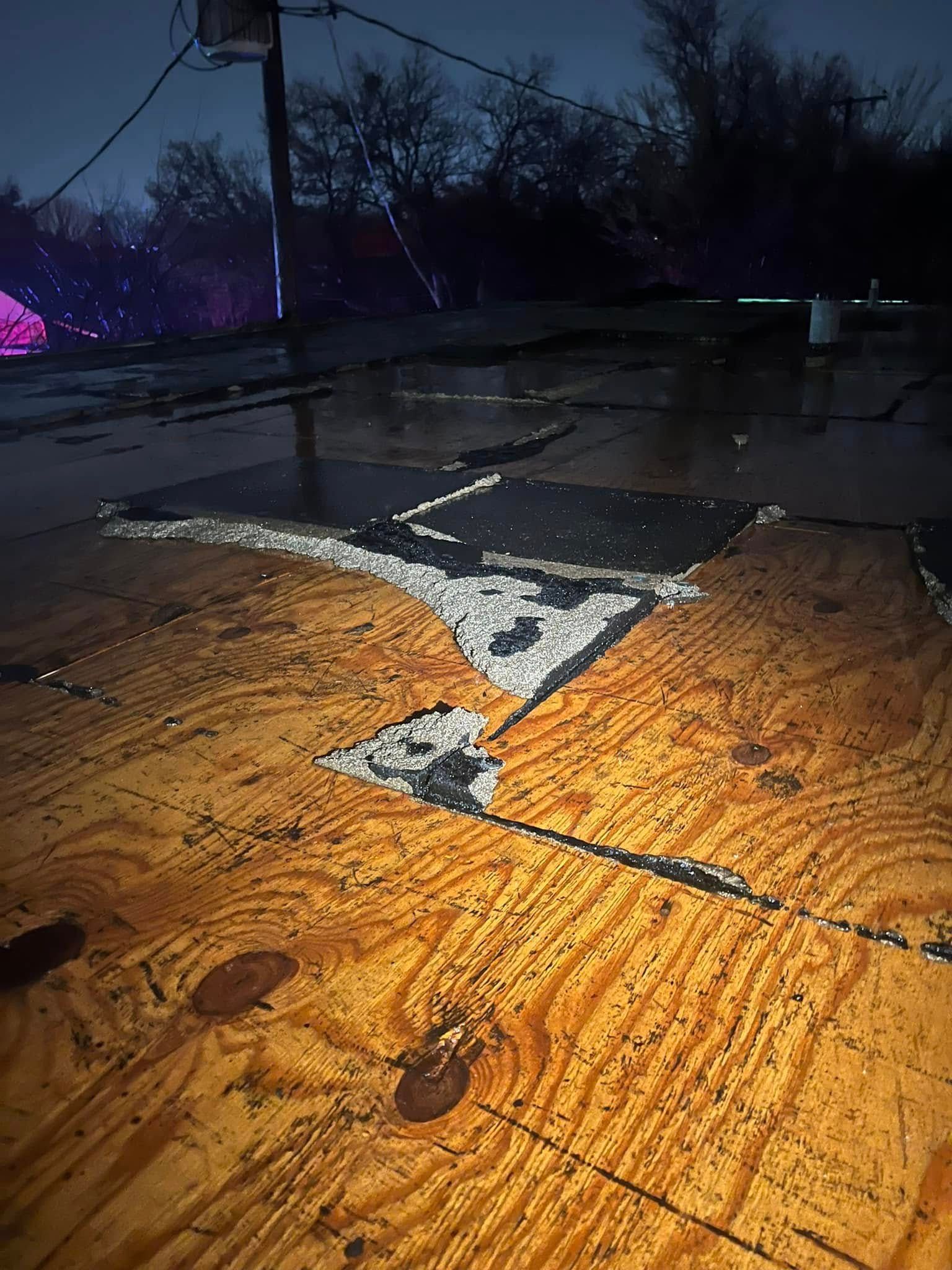 Wet rooftop at night with a damaged black patch and reflective puddles under dim purple light.