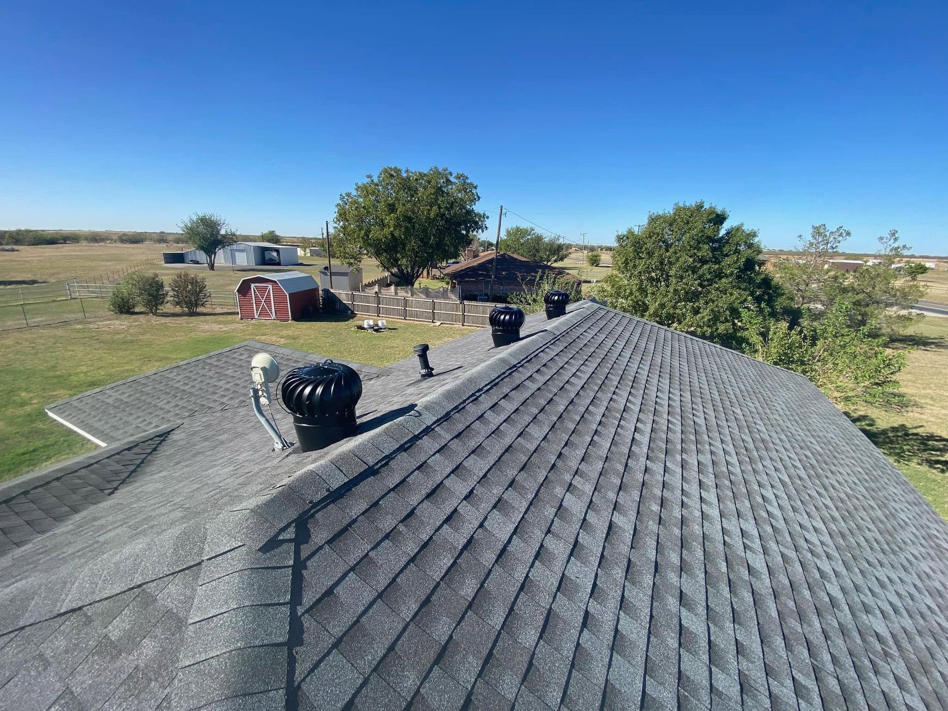Roof shingles with rooftop vents in a rural landscape under a clear blue sky
