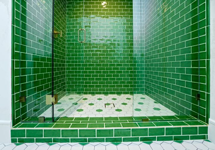 Green-tiled shower stall with white floor tiles and a glass enclosure