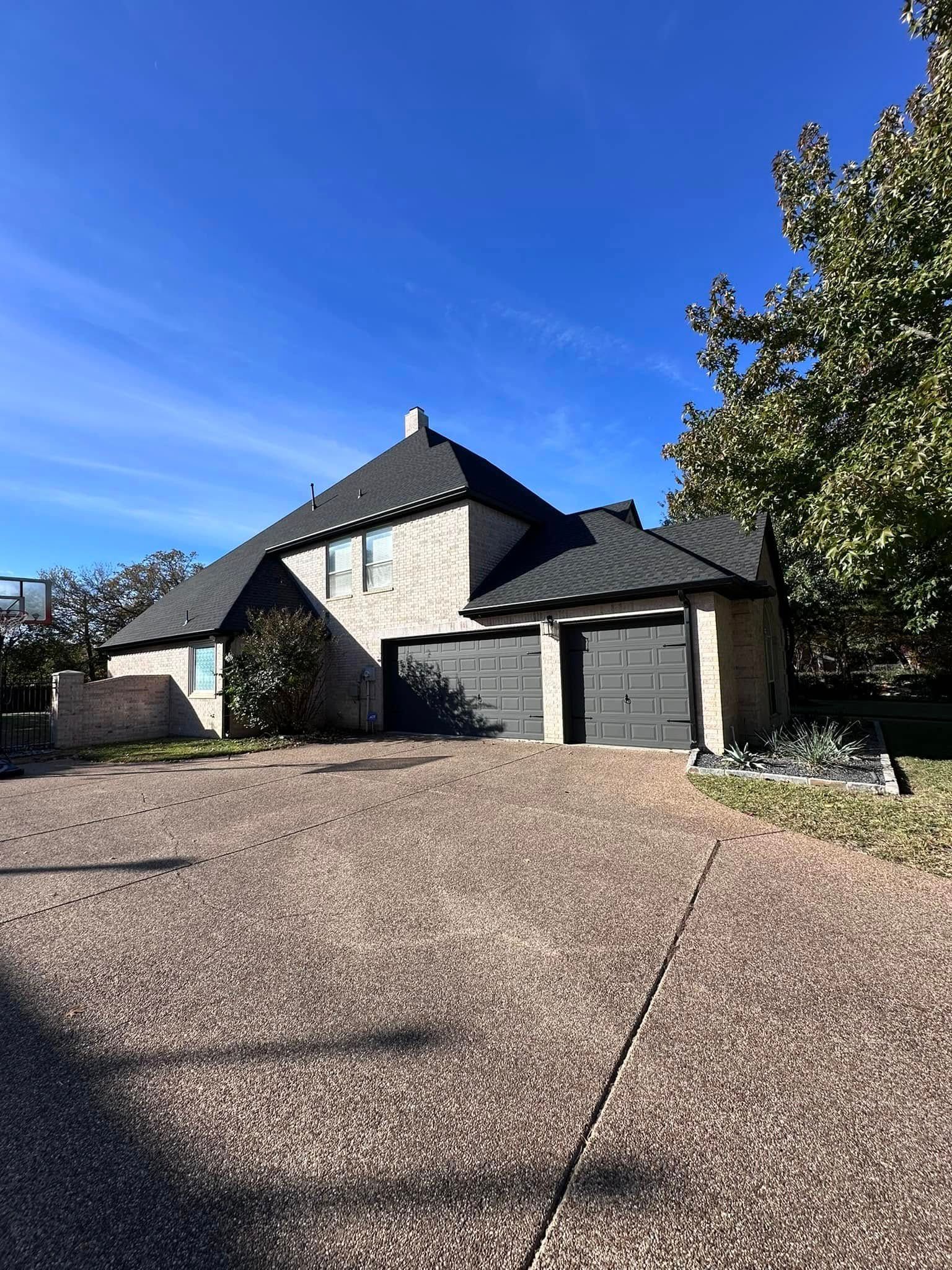 Modern stone house with a gravel driveway, dark roof, and blue sky