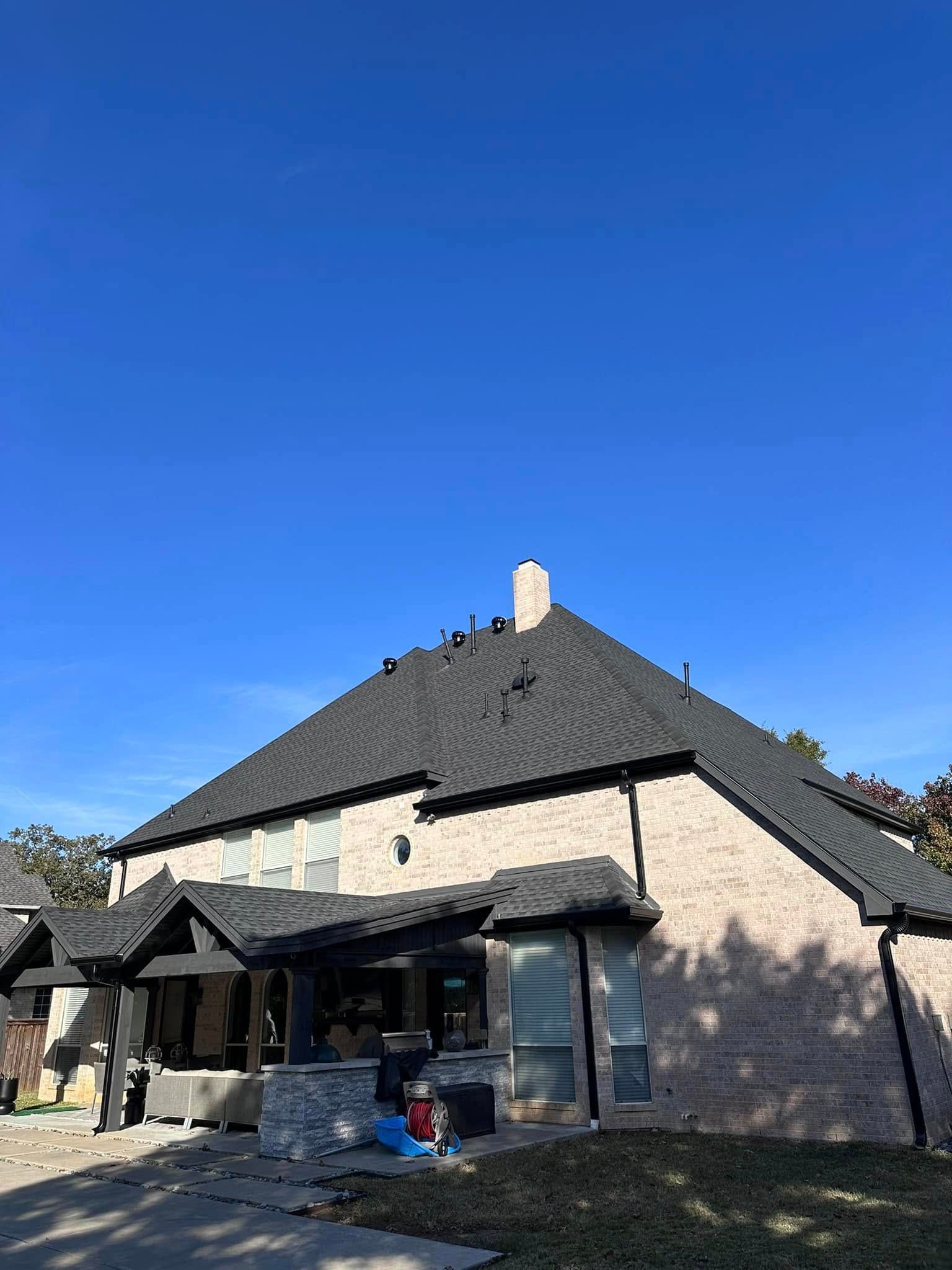 Stone house with a steep dark roof and patio under a clear blue sky