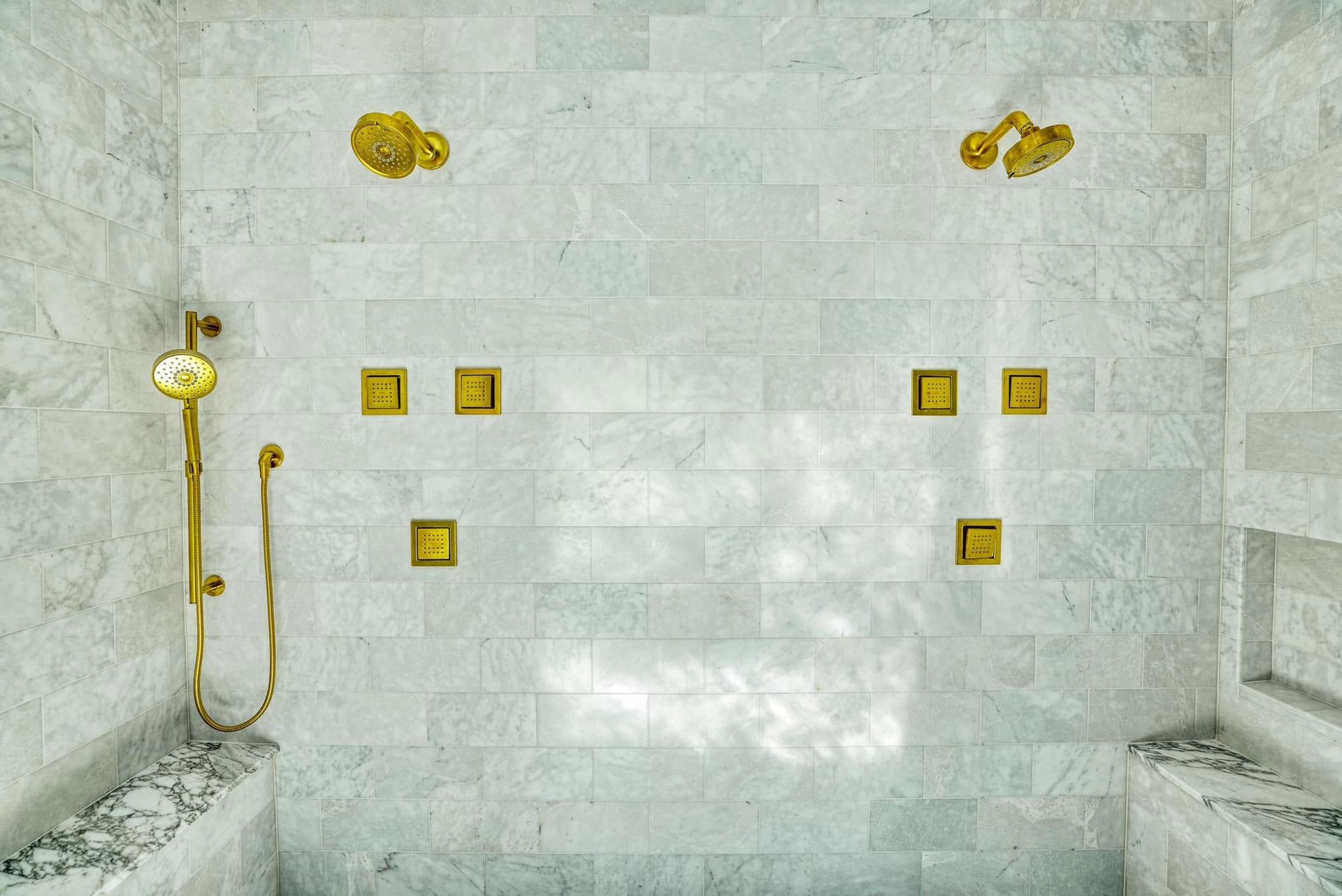White marble bathroom with gold shower fixtures and wall-mounted controls