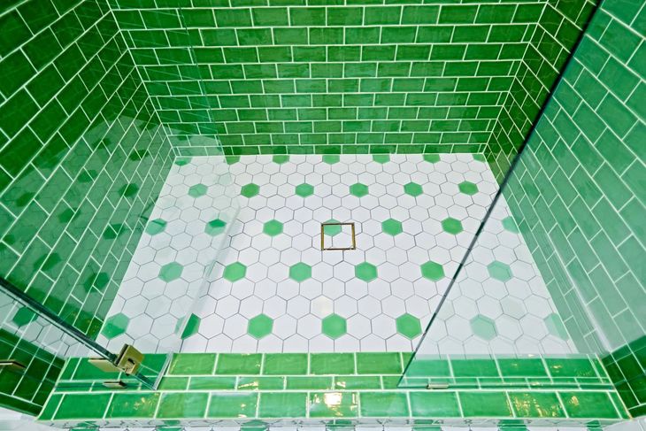 Green-tiled shower stall with white hexagonal floor tiles and a drain in the center.